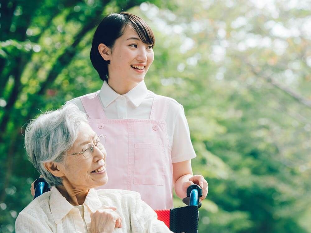 自然の中にいる車椅子に乗った高齢女性と女性ヘルパー