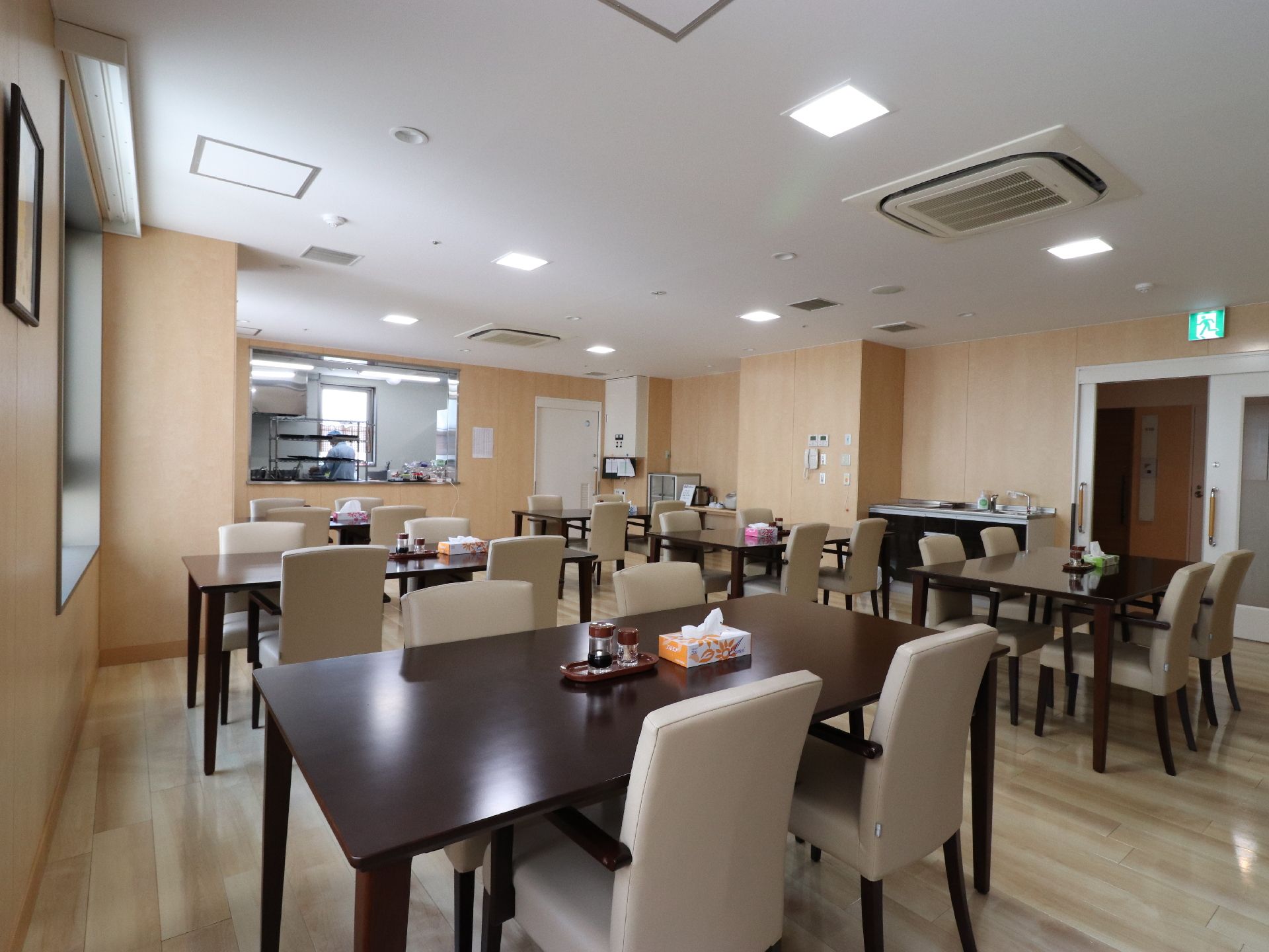 食堂の入り口は、白いスライド式のドアがついている。テーブルと椅子の脚と肘おきはこげ茶で色調が同じである。