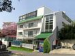 建物は3階建てで、屋上にも一部施設があるように見える。入口付近には自動販売機があり、周囲は木々や花に囲まれている。