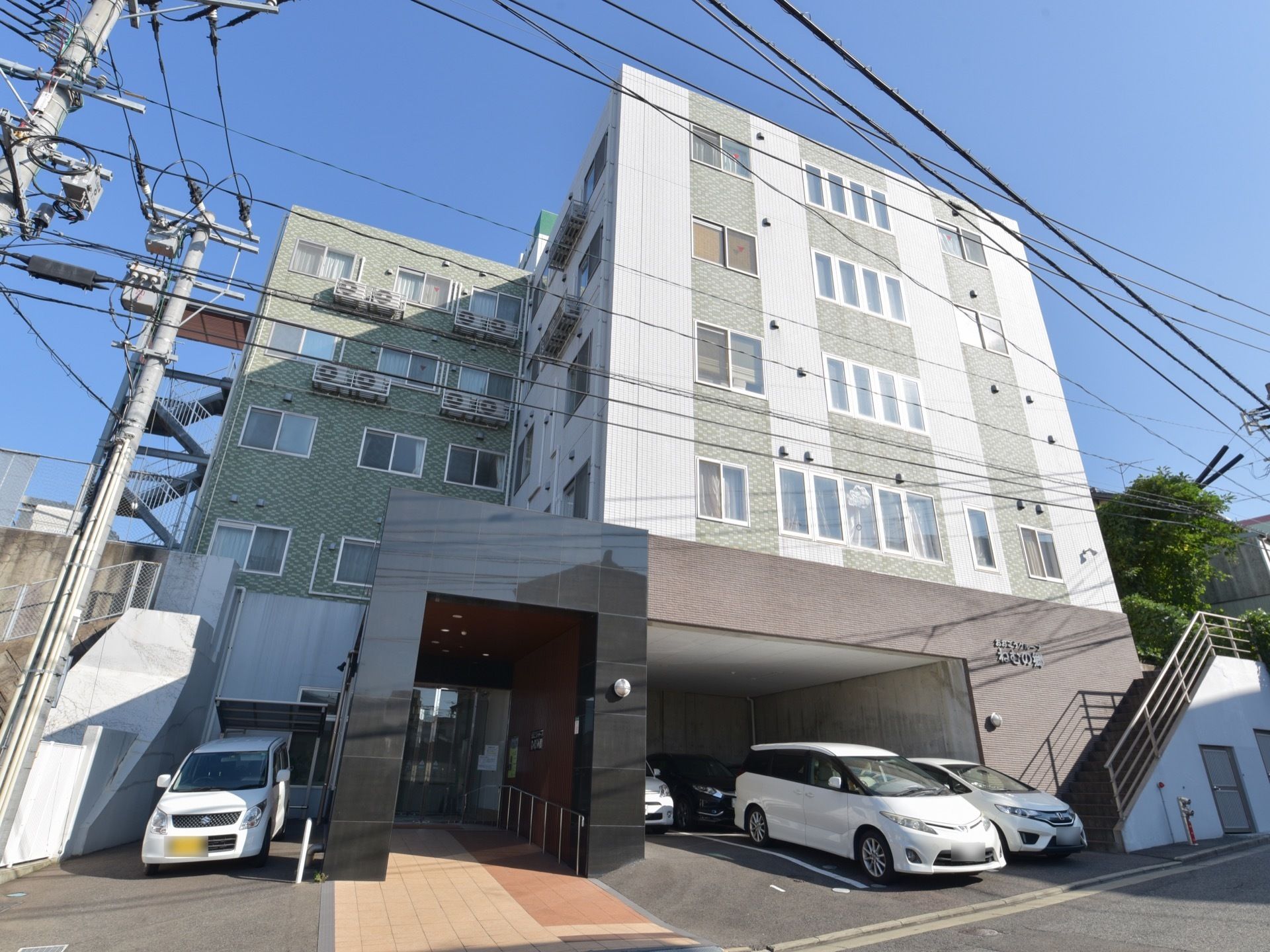 レンガ張りの建物の下が駐車場になっている。ゆるやかなスロープを進むと玄関がある。右側に階段も設置されている。