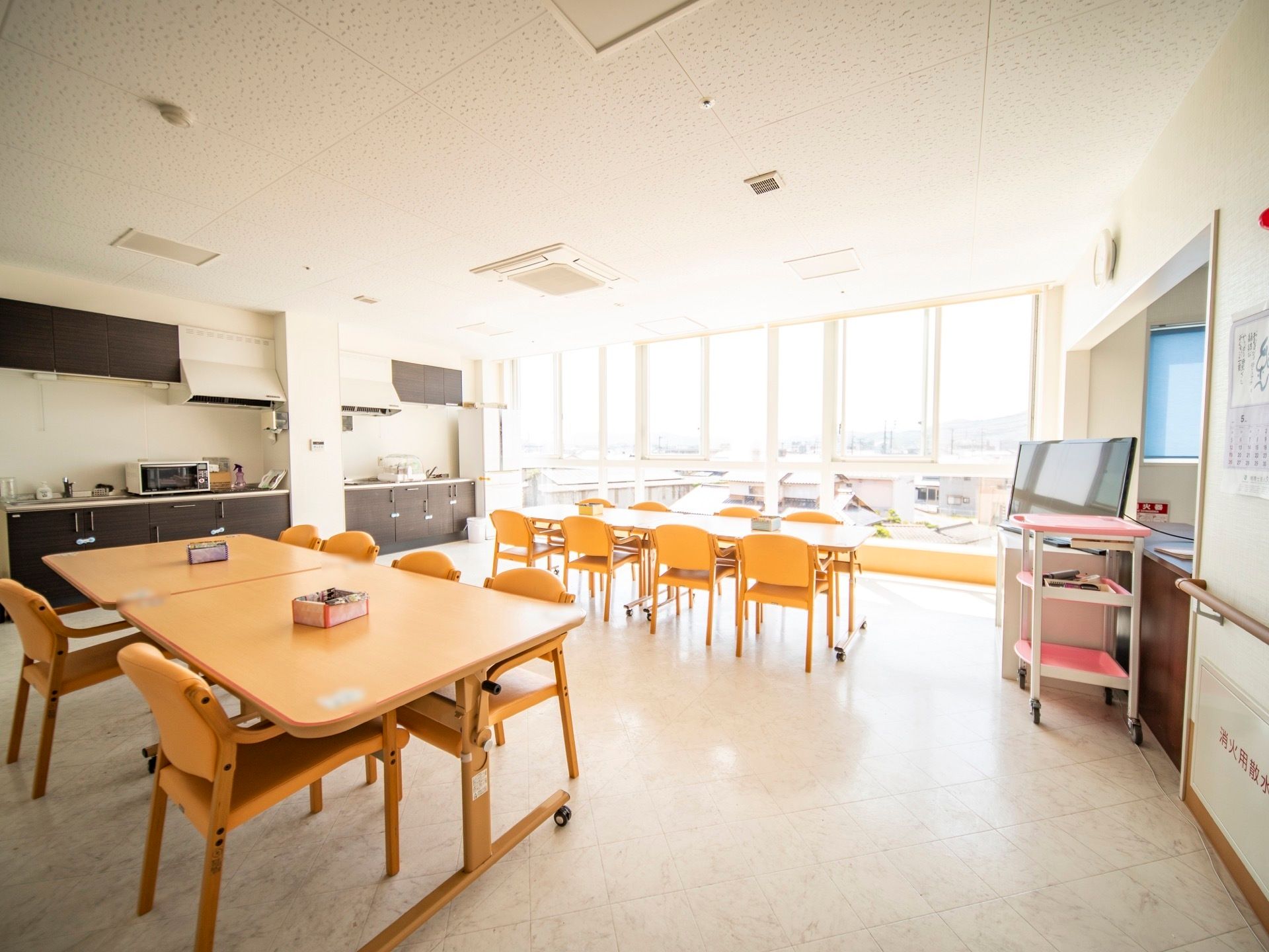 食堂から窓越しに近くの家並みが見える。壁際に柱をはさんでキッチンがあり、レンジフードが2つ設置されている。