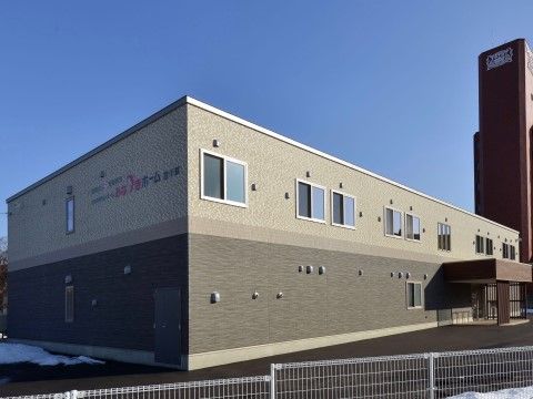 二階建ての施設外観である。最寄り駅から徒歩６分に位置しており、24時間看護師が常駐している。施設内には駐車場が完備されている。