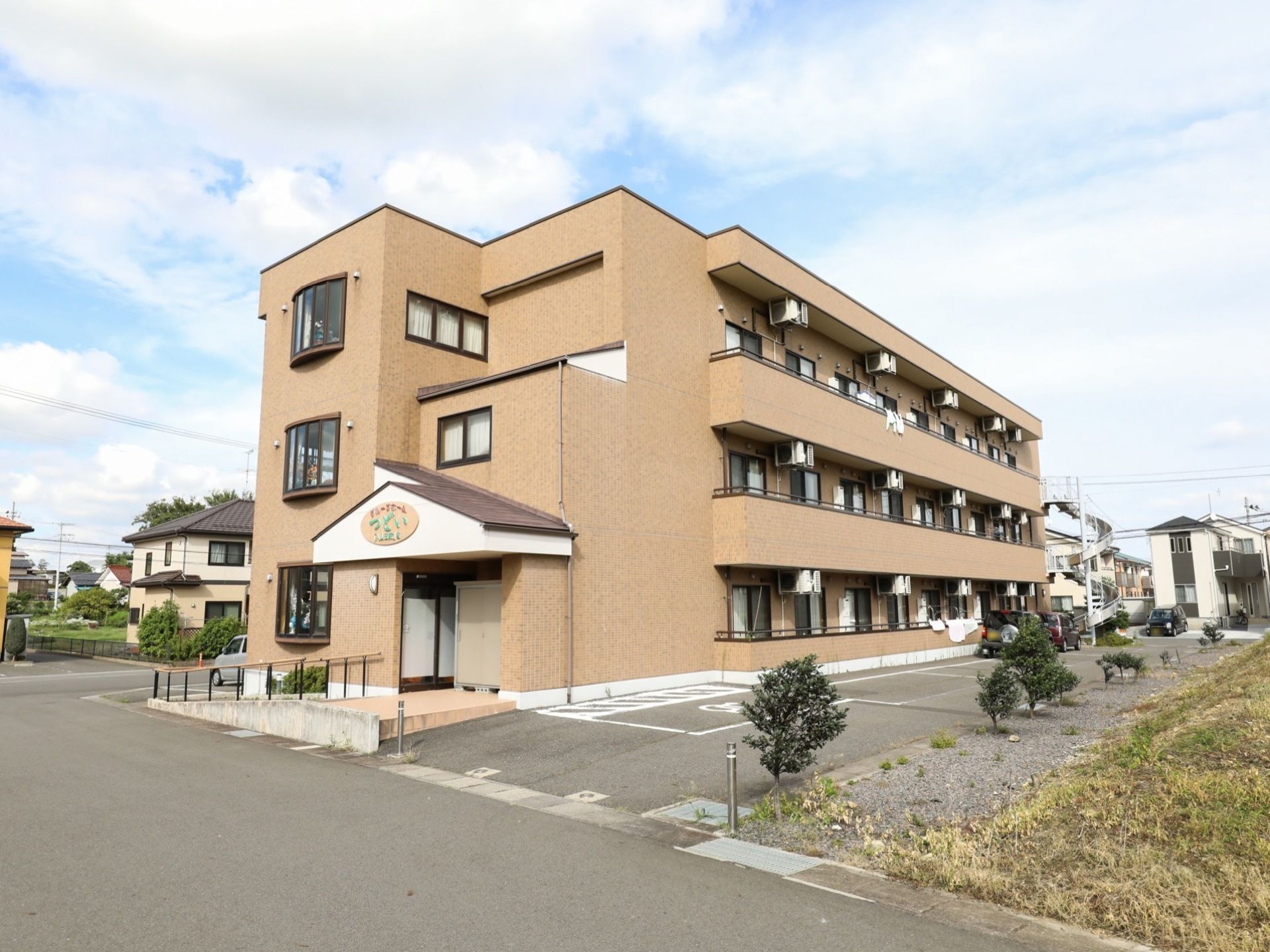 ゆったりとした敷地に佇む施設は３階建てで、１階の玄関前には手すり付きのスロープが設置されている。また、広い敷地内には駐車場を完備している。