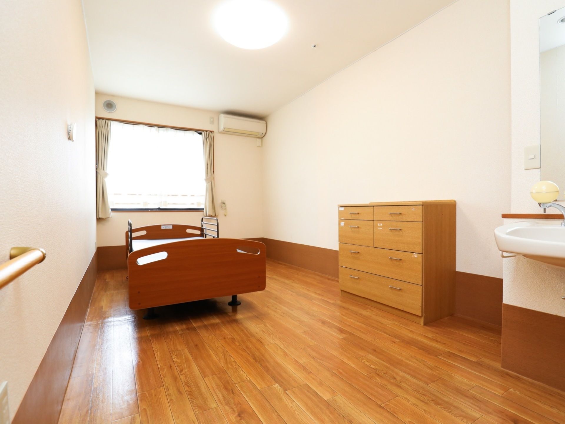 白と木目調をモチーフとした落ち着いた雰囲気の居室である。ベッド、収納タンス、洗面台、空調が備えつけられている。