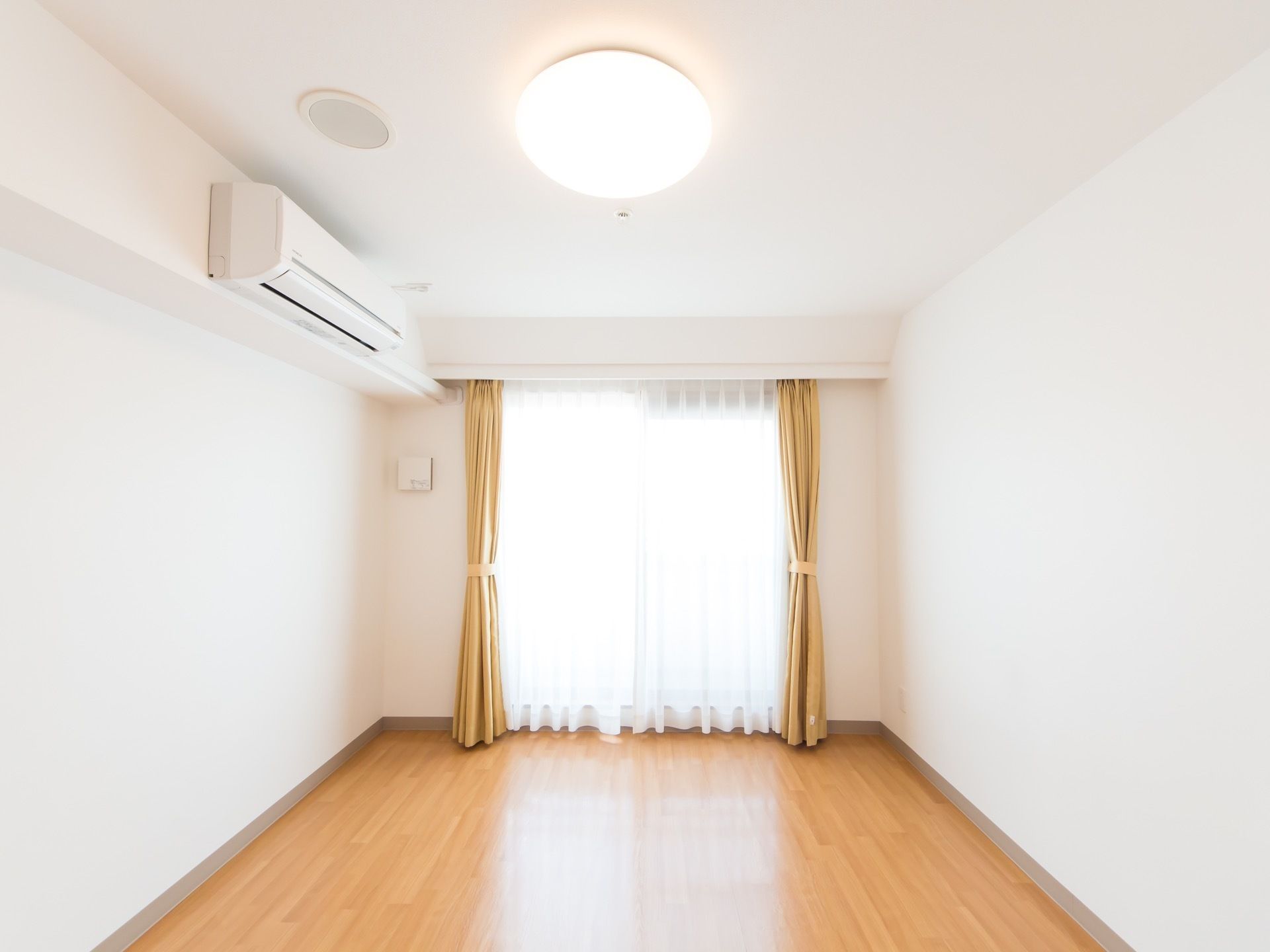 白を基調とした日当たりのよい居室である。生活に最低限必要なエアコンやLEDライト、カーテンが完備されている。