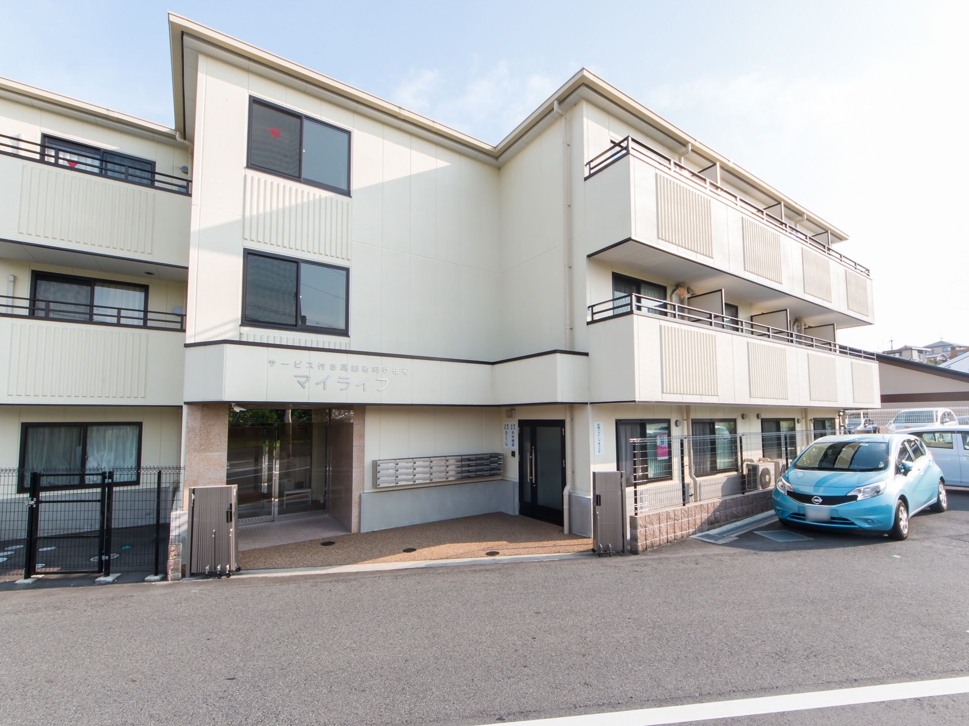 ３階建てのおしゃれな建物である。２、３階部分にはベランダが完備されている。建物の横には駐車場がある。
