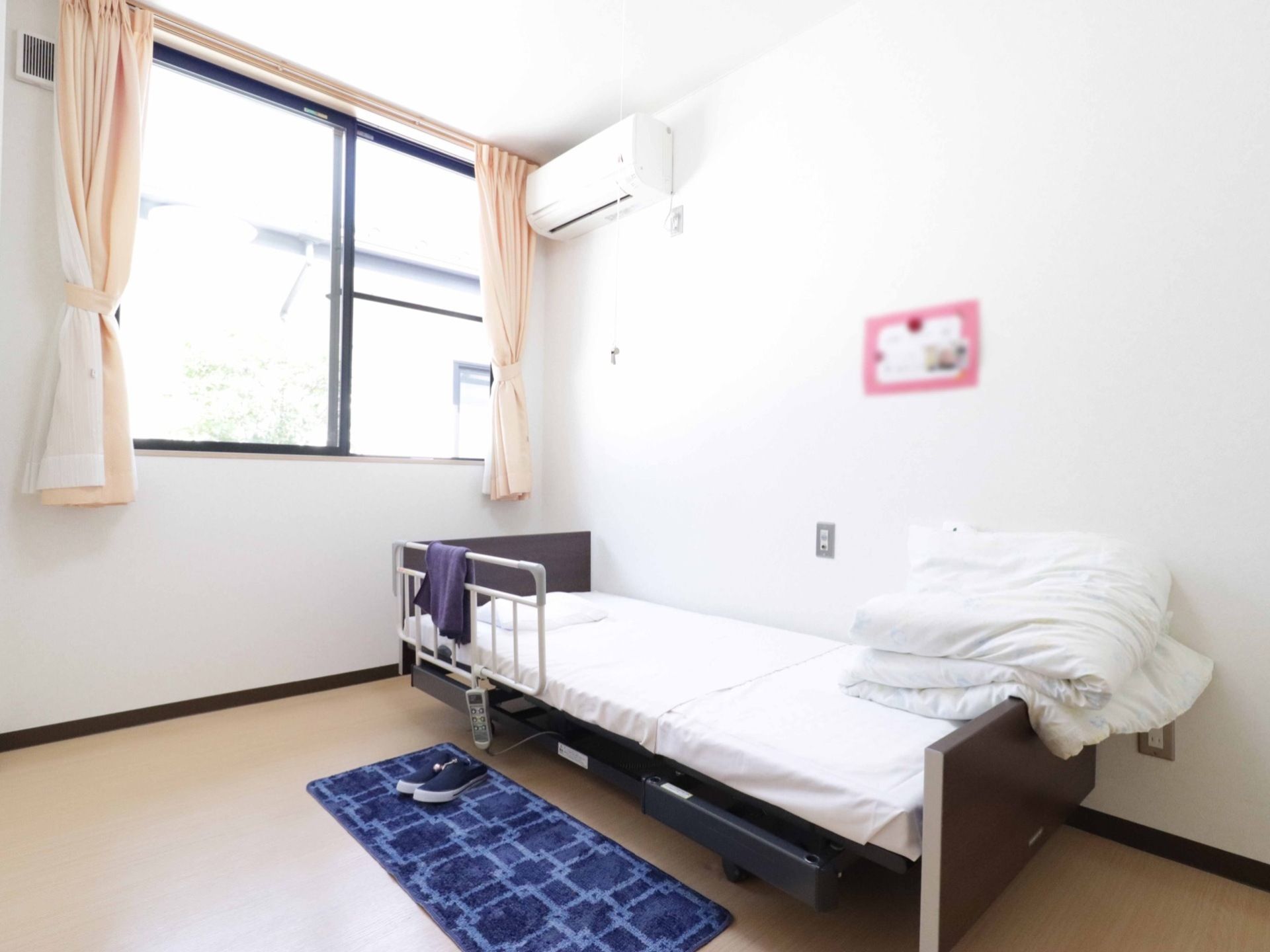 窓から陽が良く差し込んでいる居室は壁も白くとても明るい。電動の介護ベッドがありボタンで操作できるので、入居者様本人でも安心して利用できる。