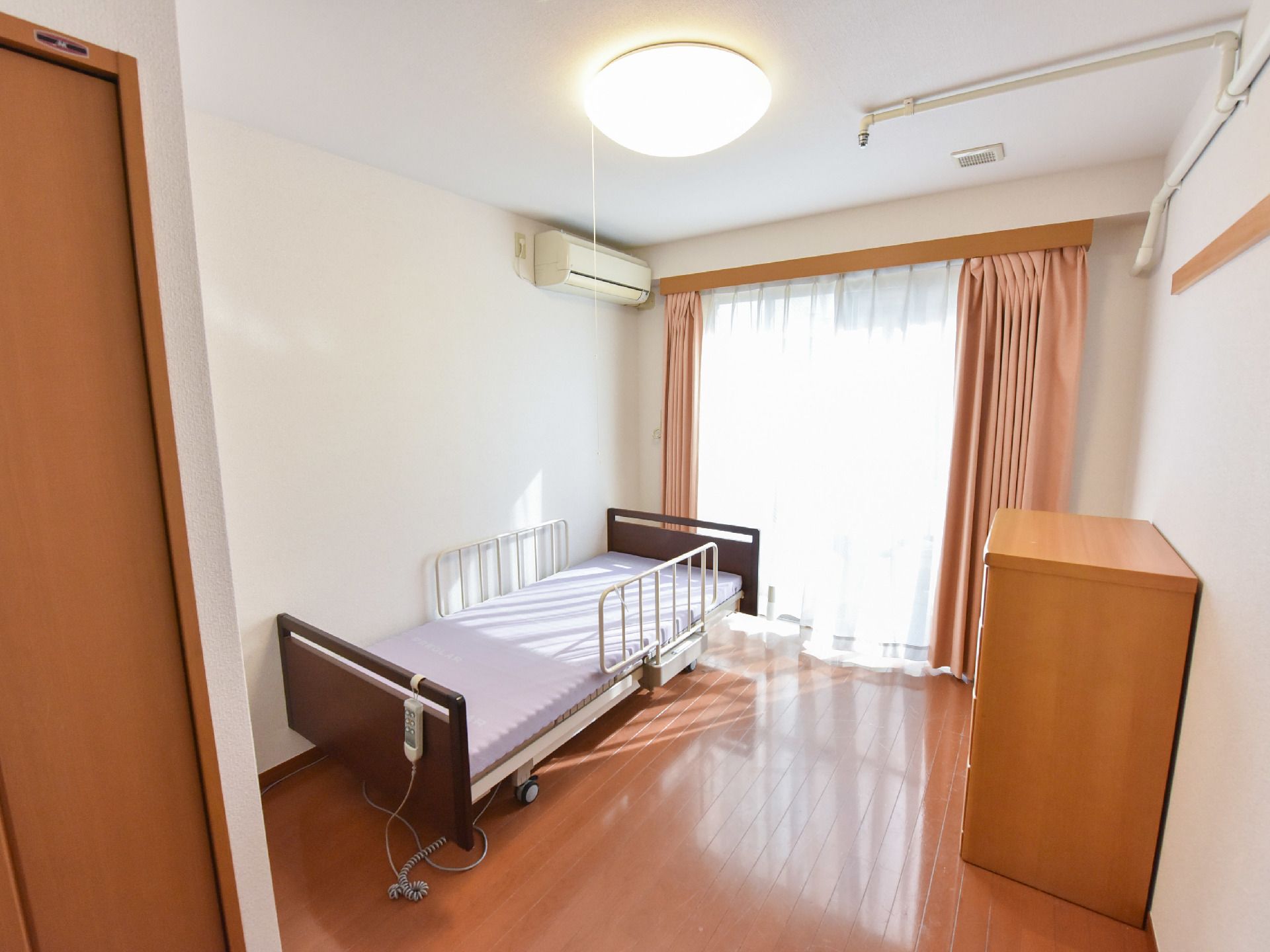 部屋にはベッドと空調機があり、フローリングタイプである。カーテンを開けると日差しが入ってくる。また、換気扇も装備されている。