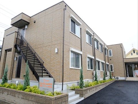 茶色のタイルを張った２階建て建物に、黒い外階段が付いている。壁面から通路を空けて、低い壁で囲った植え込みを作っている。