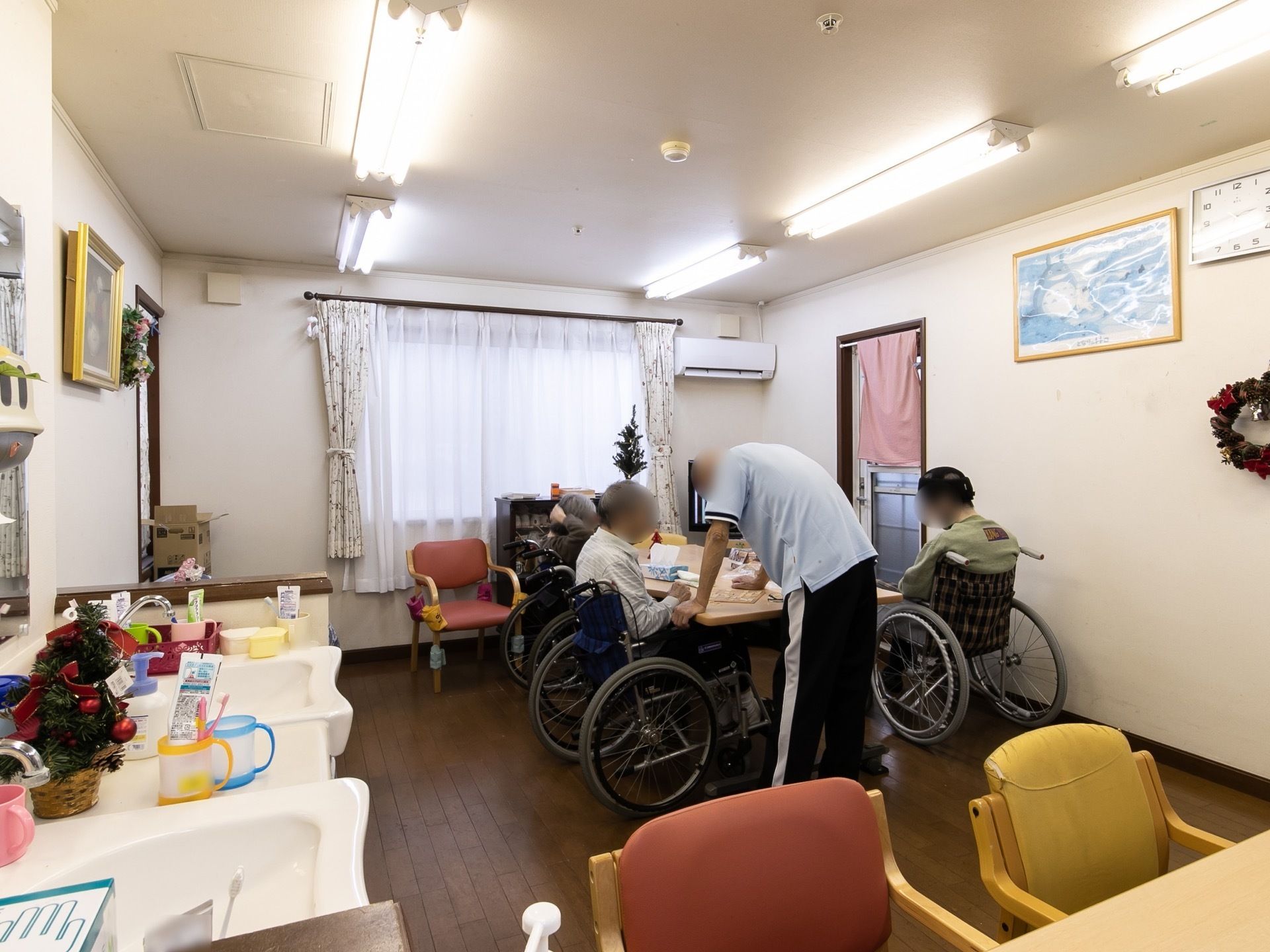 フットレスタイプの洗面台が備えつけられたリビングで、車椅子に座った入居者様とスタッフが話をしている。