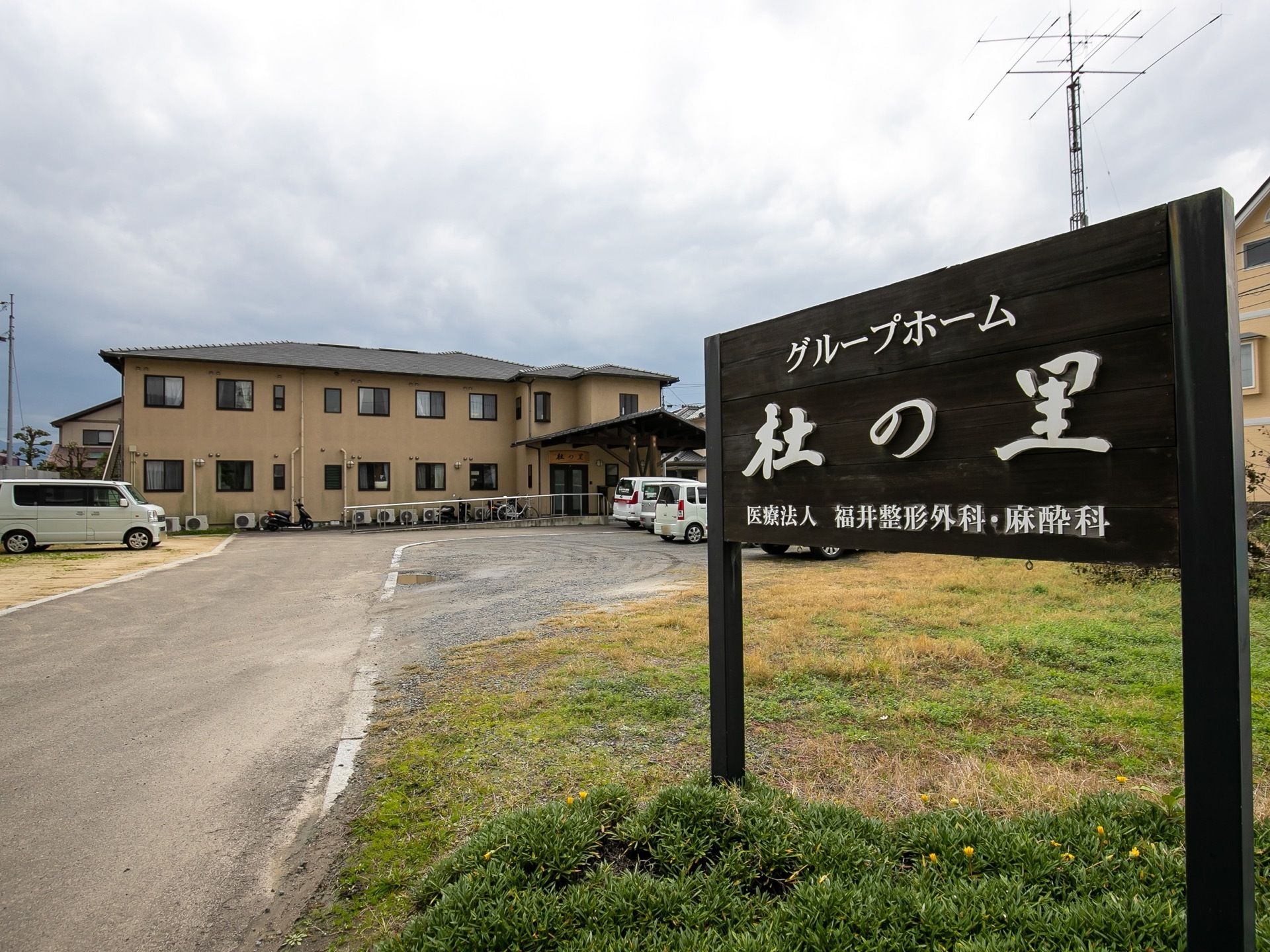 ２階建てのベージュが基調の２階建ての建物である。敷地内は広く、駐車場や芝生の生えた空き地が広がっている。