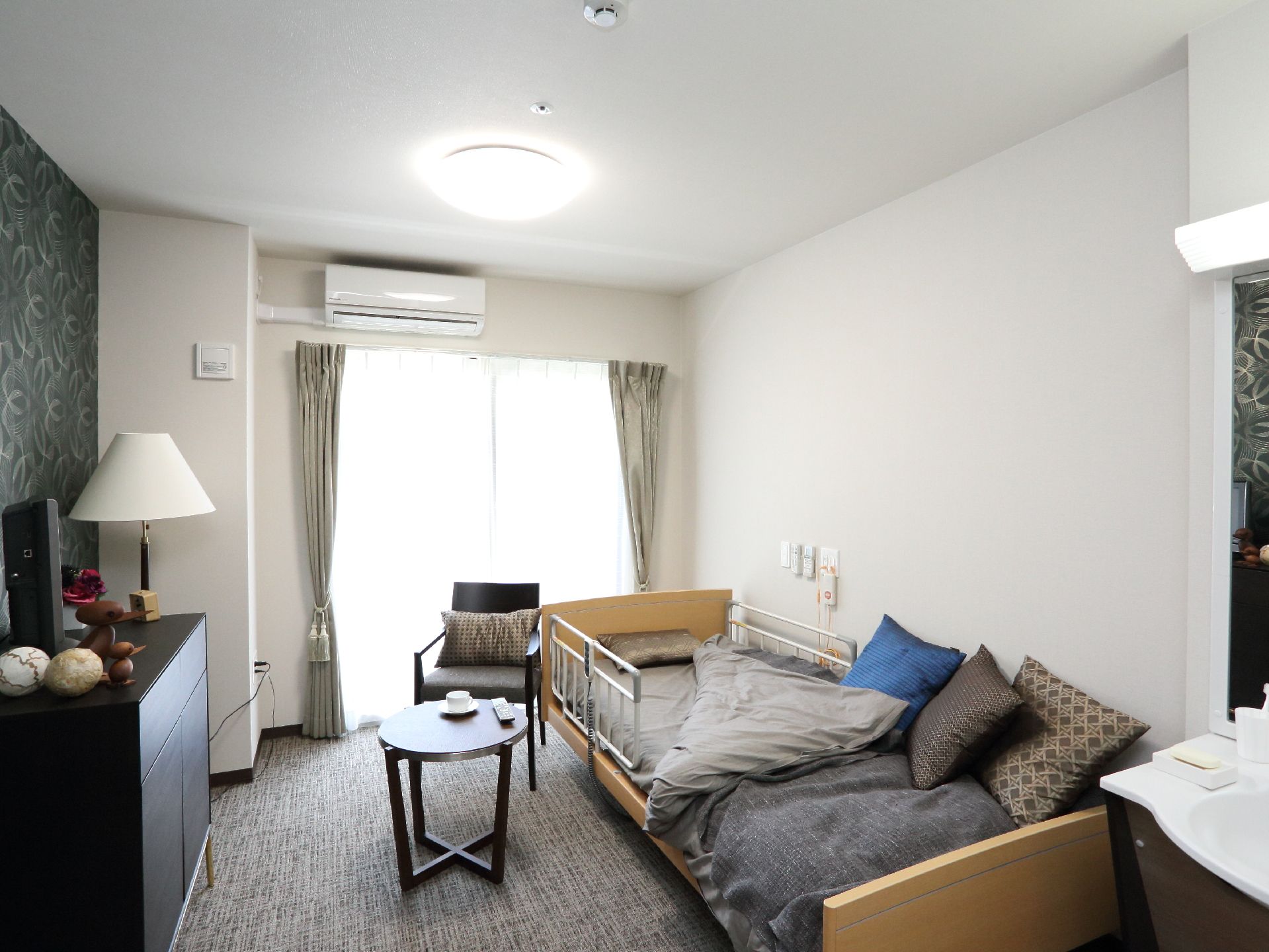 ワンルームタイプの居室はグレーを基調としたモダンな部屋。ベッドを置いてもゆとりのある広さがある。エアコンが設置してある。