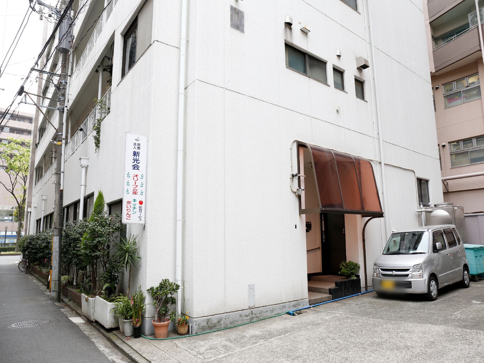 施設は6階建ての白いビルの中に設けられている。ビルの壁に白地の施設の看板がかかっていて、道路沿いには緑が育てられている。