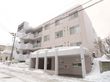 建物は4階建てになっていて、道路に面している。左側には外階段がある。外玄関周辺には屋根が付いていて、そばの壁には手すりが付いている。