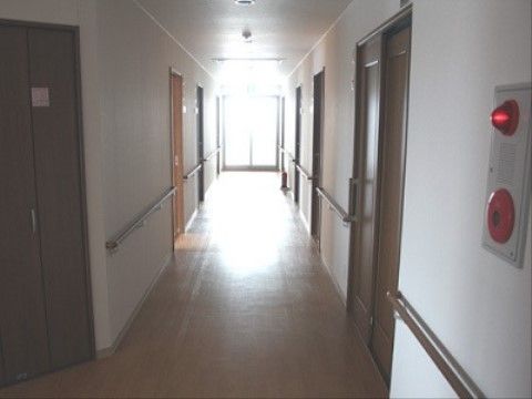 白い壁に手すりが設置され、自動火災報知設備がある。木目調の引き戸式ドアがある。窓から光が差し込み明るい。
