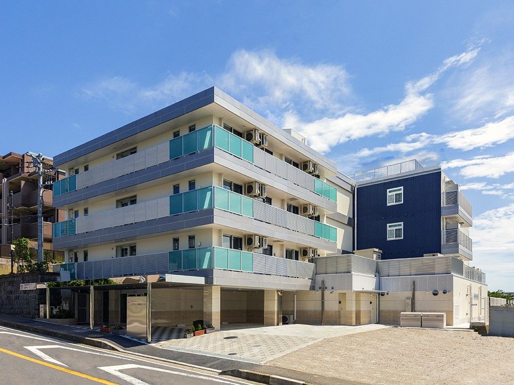 ライトグレーを基調とした４階建ての建物である。建物の前と１階部分には駐車場があり、ご家族が来訪する際も安心である。