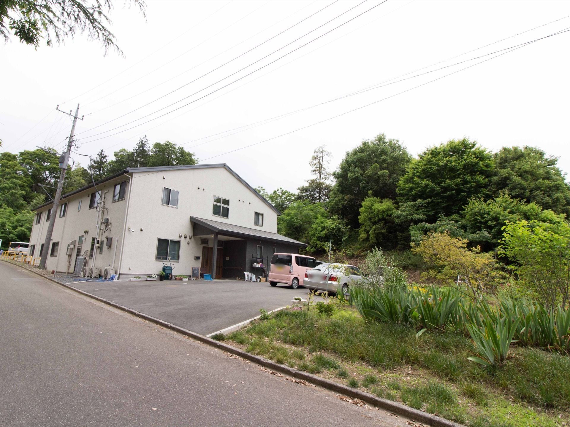斜め方向から、建物全体とその周辺を写したものである。２階建ての施設の周りには、背の高い大きな木が何本も立っている。