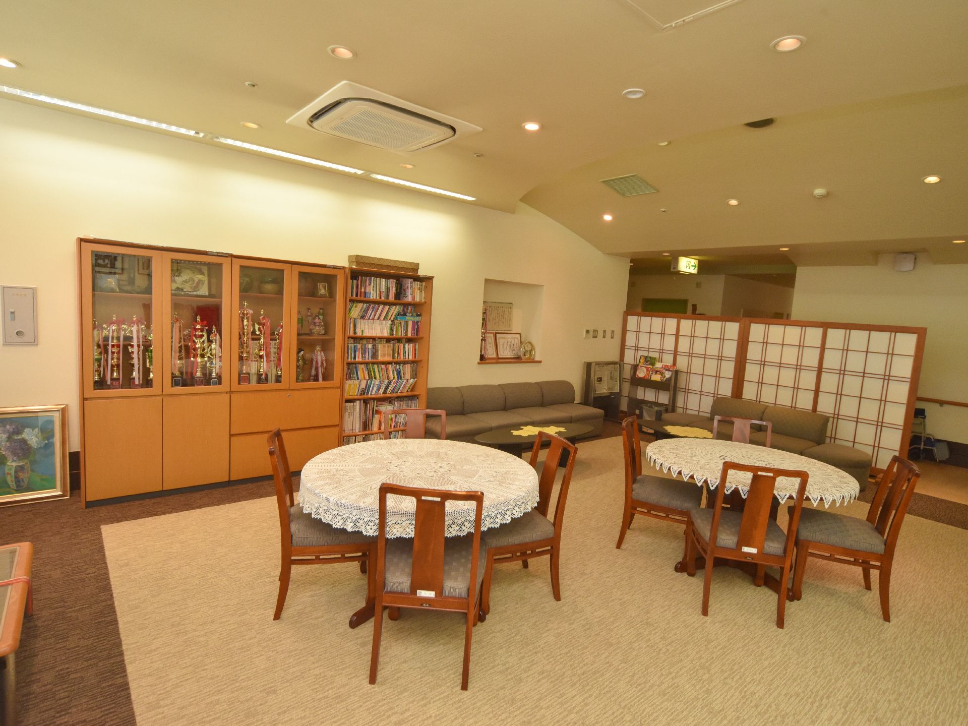 多目的室の壁際には、ブラウンの収納家具や本棚などが置かれている。中央には、丸いテーブルが2台ゆったりと並べられている。