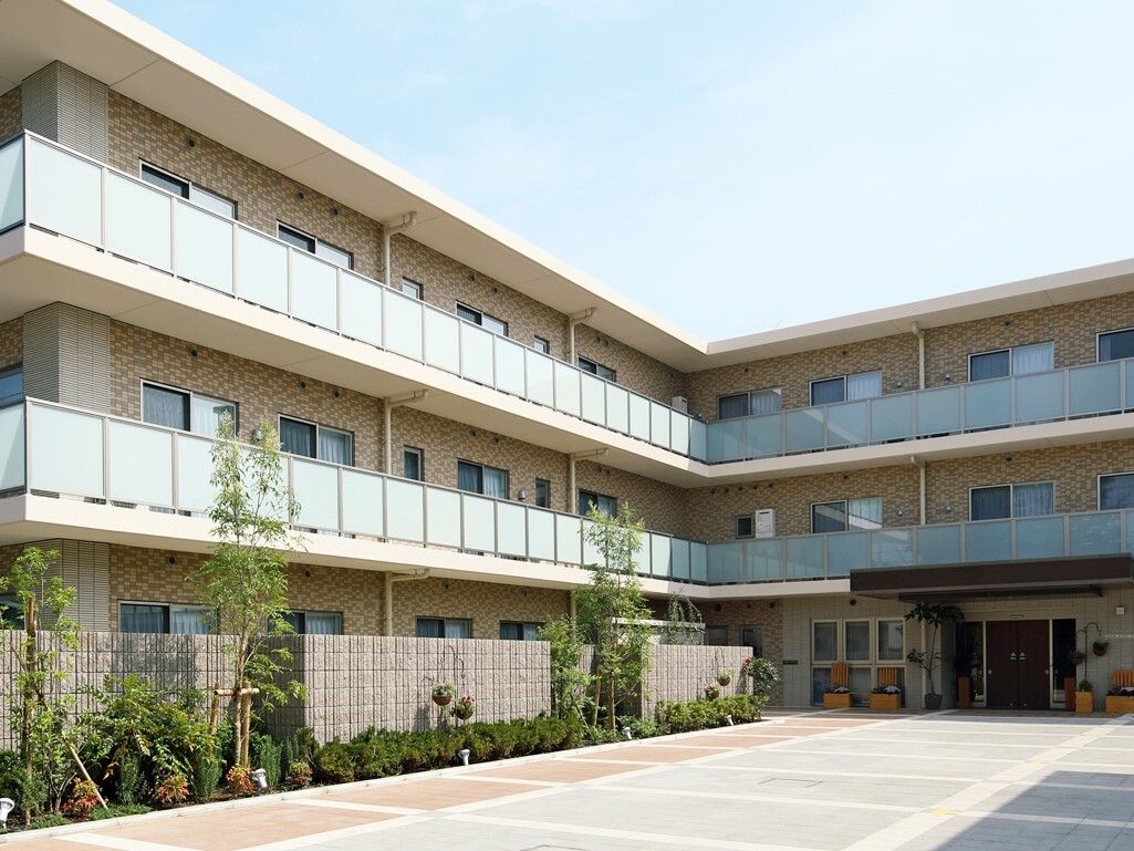 施設は3階建て。塀に沿って緑が植えられ、マンションのような造りになっている。入り口は本通りから離れたところにある。