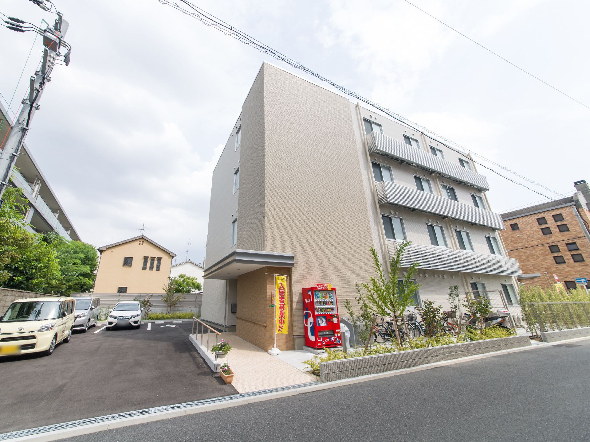 施設の建物は4階建てで、2階以上にはベランダが設置されている。玄関前にはスロープがあり、その右側には自動販売機が設置されている。