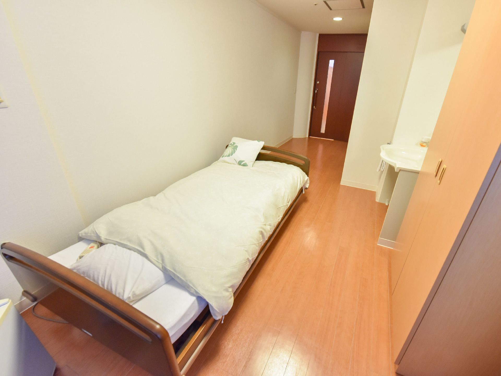 居室には電動の介護ベッドが置かれている。部屋はバリアフリーでドアには明かり取りの細長い窓が付いている。