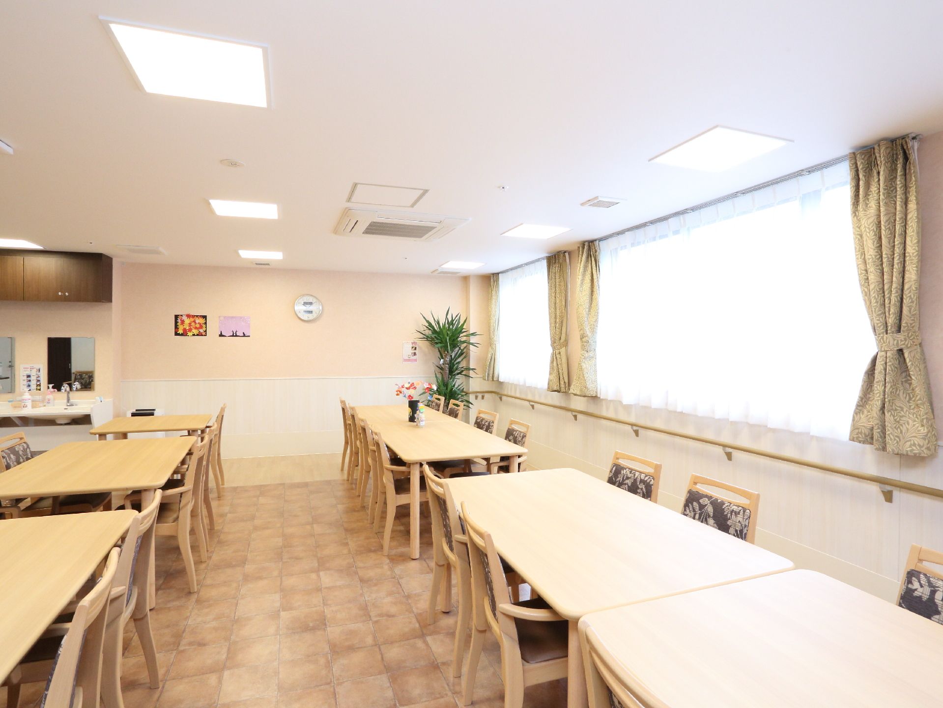 窓がたくさんある明るい食堂には観葉植物が置かれている。壁には絵や時計があり、洗面台も設置されている。