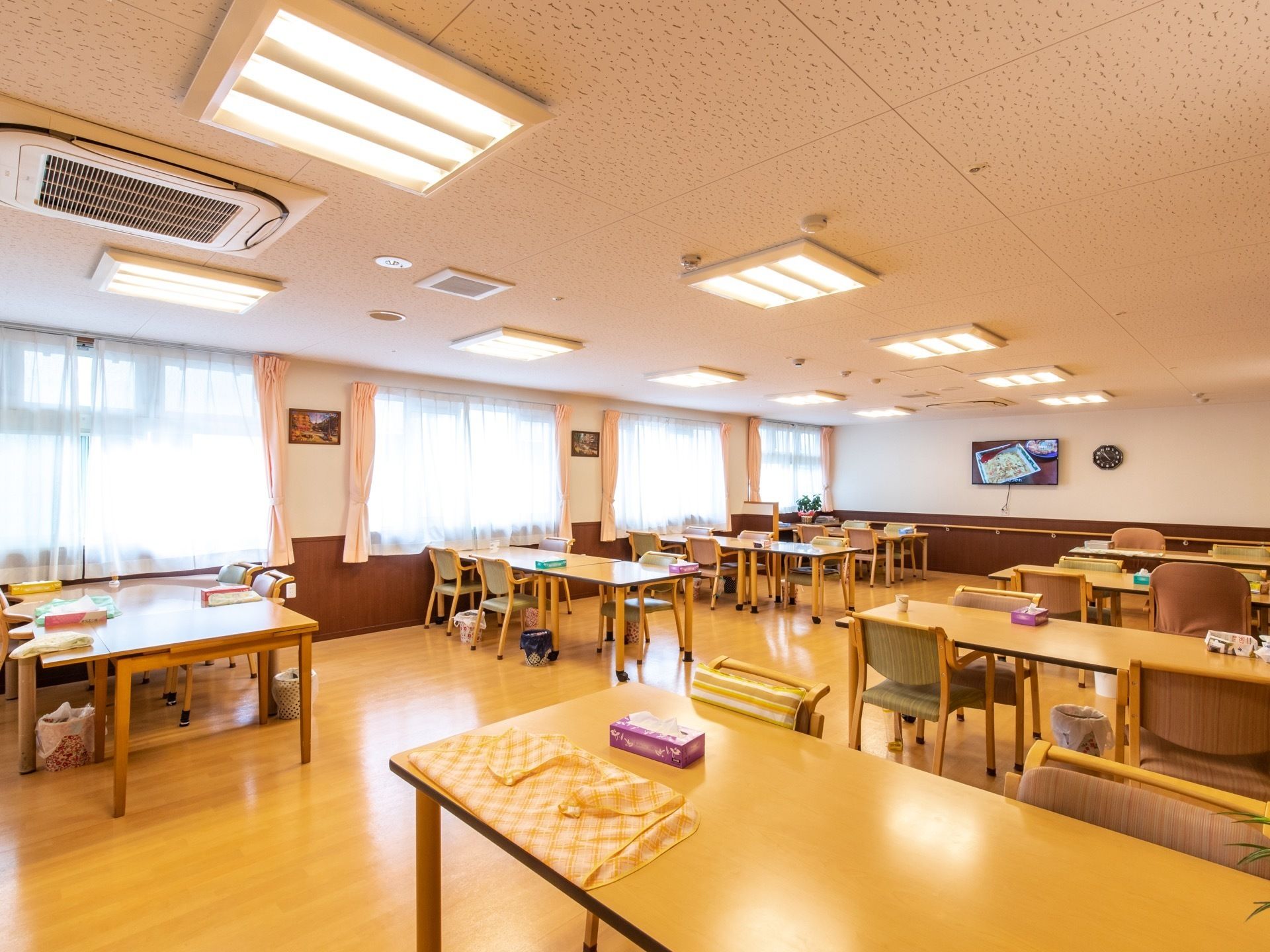 食堂はゆったりとした広さがあり、テーブルや椅子がたくさん並べられている。右側には窓が取りつけられており、ピンク色のカーテンが掛けられている。