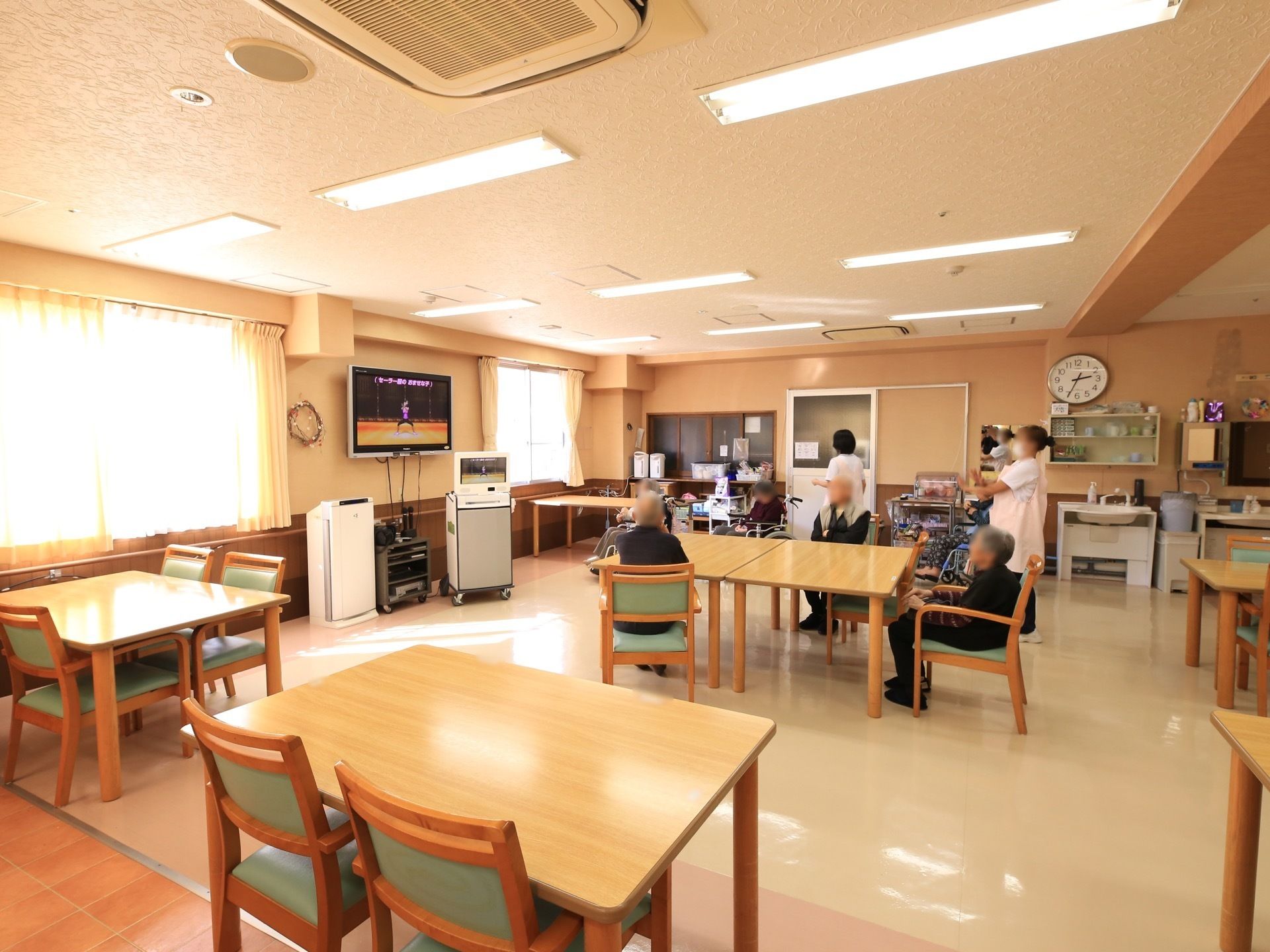 窓から日射しの差し込む明るい食堂である。４人掛けのテーブルセットや大型液晶テレビ、CDコンポが取り揃っている。