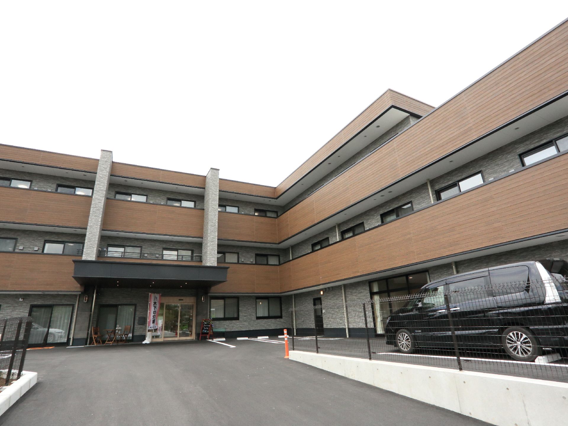 出入口正面に黒い屋根の玄関があり、建物前の広いスペースの敷地には、何台か車が止めれる駐車場になっている。