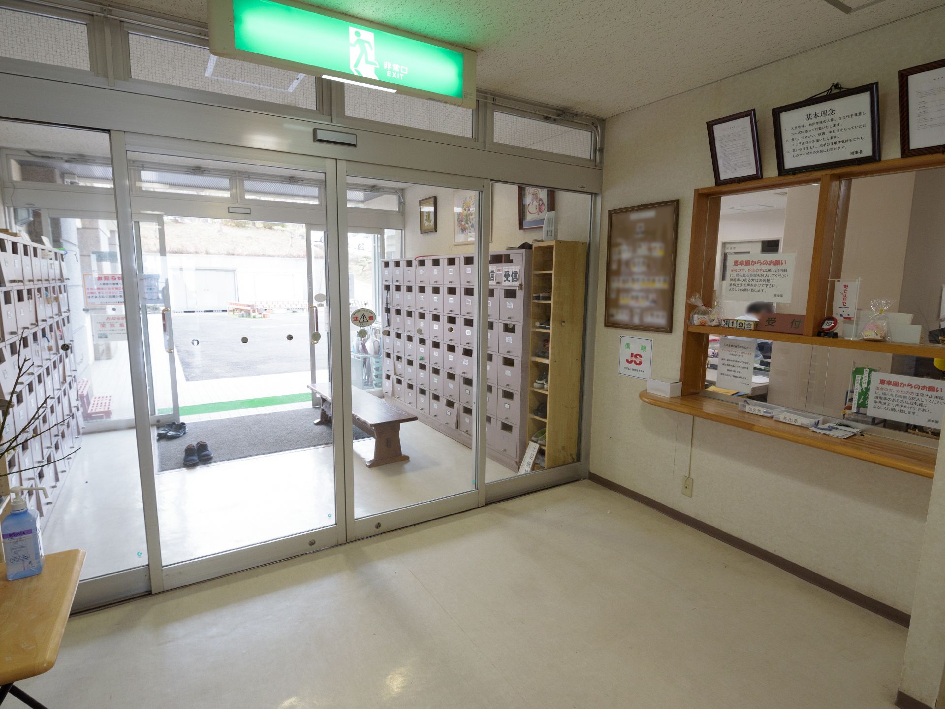下駄箱が両サイドに置かれている。受けつけの向かい側には、消毒液が置かれている。横幅にゆとりのある自動扉になっている。