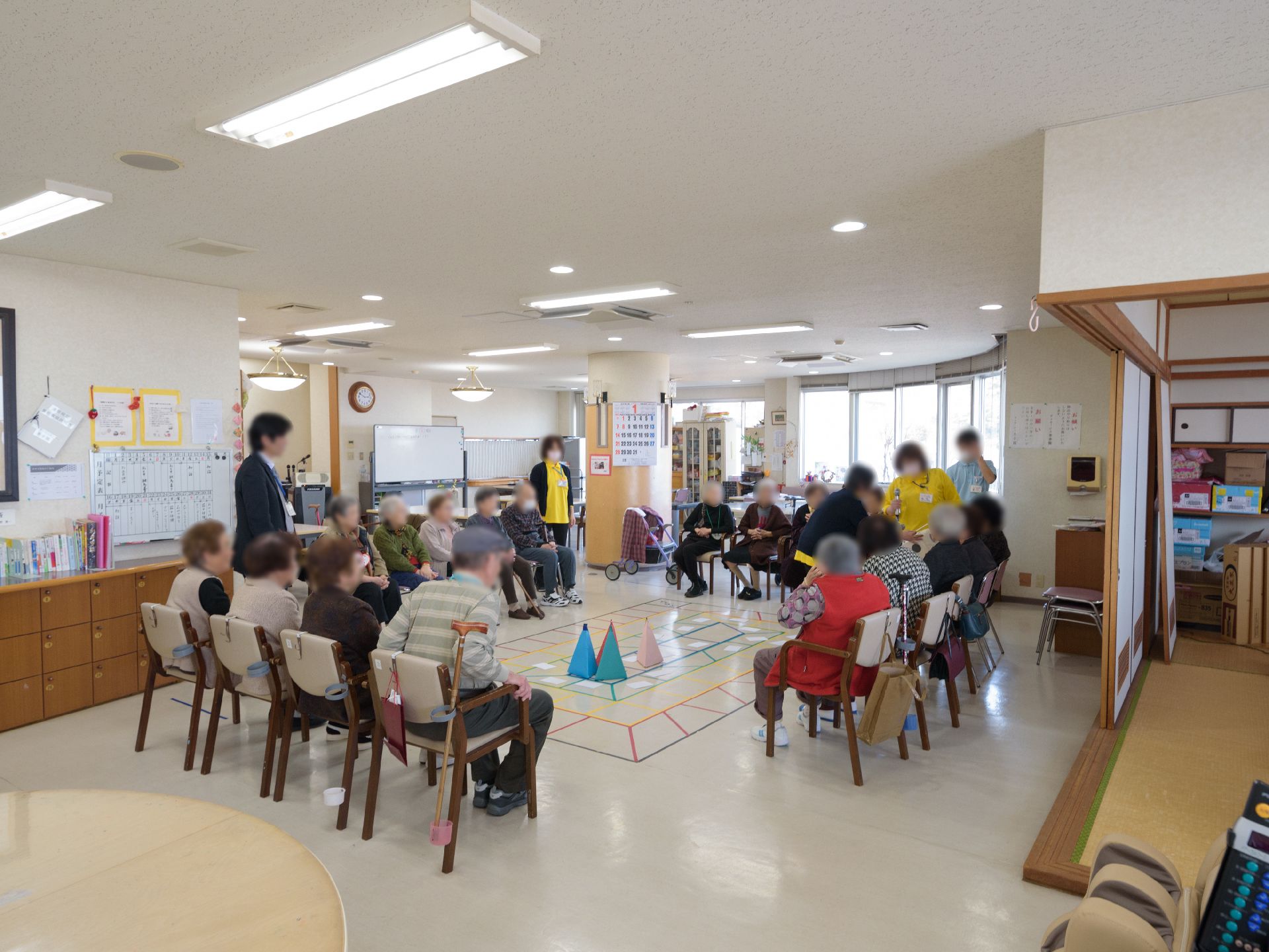 入居者様が集まり、椅子に座ってゲームを楽しんでいる。和室が併設されている。部屋の奥にホワイトボードがある。