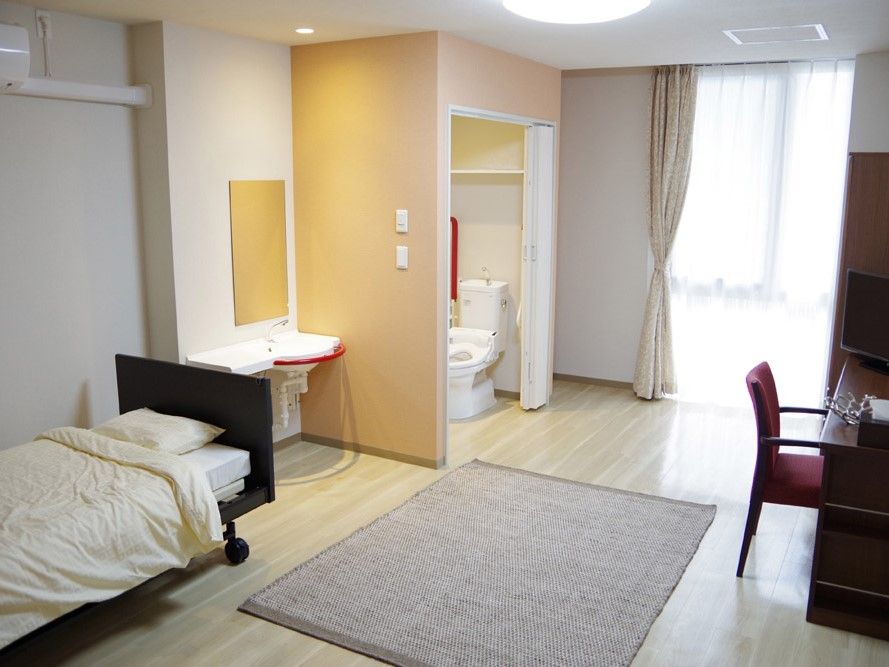 広々とした居室には窓が３ヶ所あるので日当たりがよく環境によい。介護用ベッドと２人掛けのテーブルセットが完備されている。