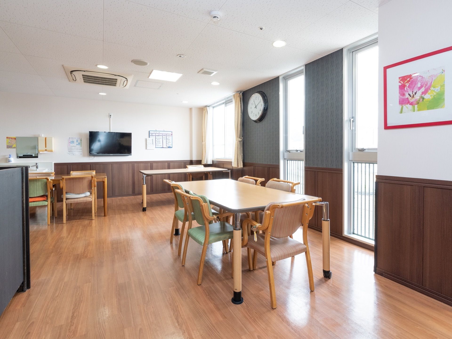 部屋の奥の壁には、大きな液晶テレビや、チラシなどが提げられている。窓際の壁には、時計や、花の描かれた絵画などが飾られている。