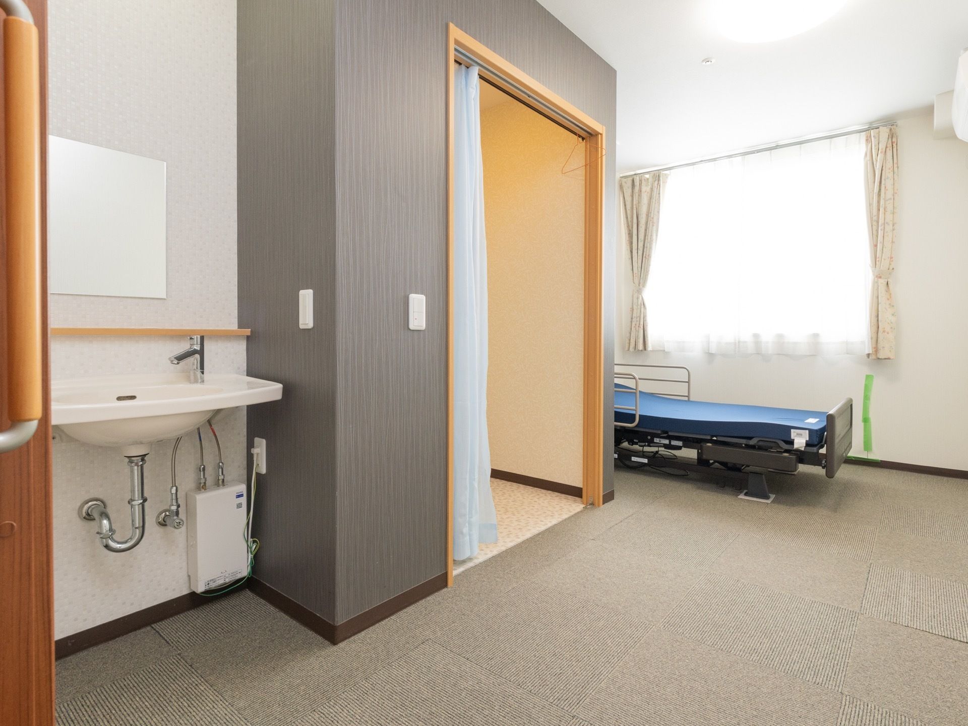 白い壁紙に、モスグレーのタイルカーペットが敷かれた、シンプルな落ち着いた雰囲気の部屋である。部屋の奥には、介護用ベッドが置かれている。