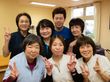 女性６人と男性１人の計７名のスタッフが２列に並んでいる。全員にこやかな顔である。右側後ろには、窓が設けられている。