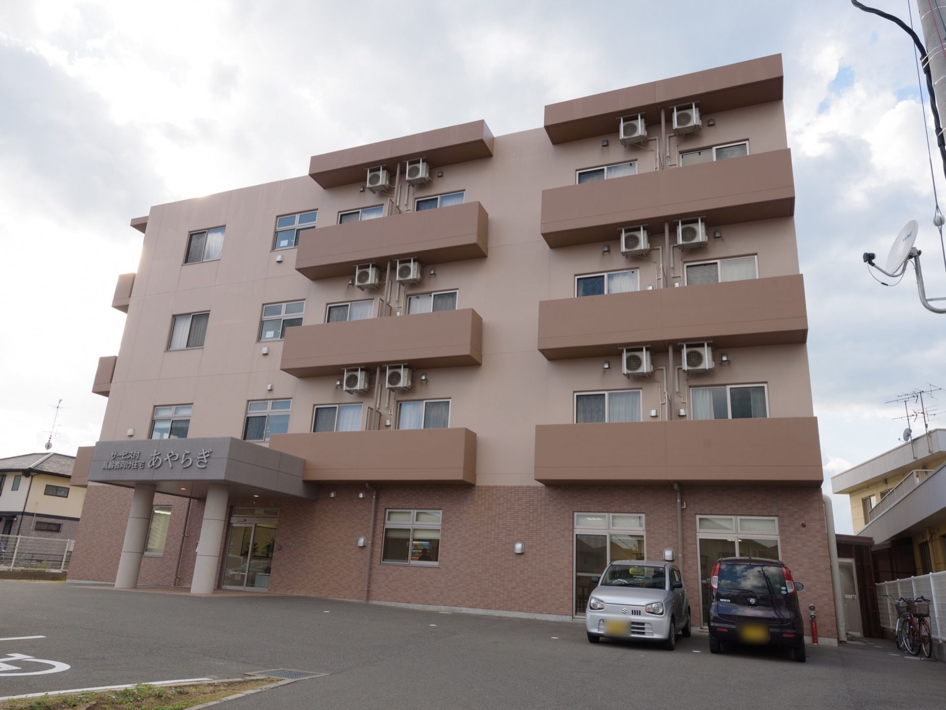 ブラウンとベージュが基調の４階建ての建物は、優しく落ち着いた印象がある。建物正面には駐車場がある。入り口に段差がなくスムーズに出入りできる。