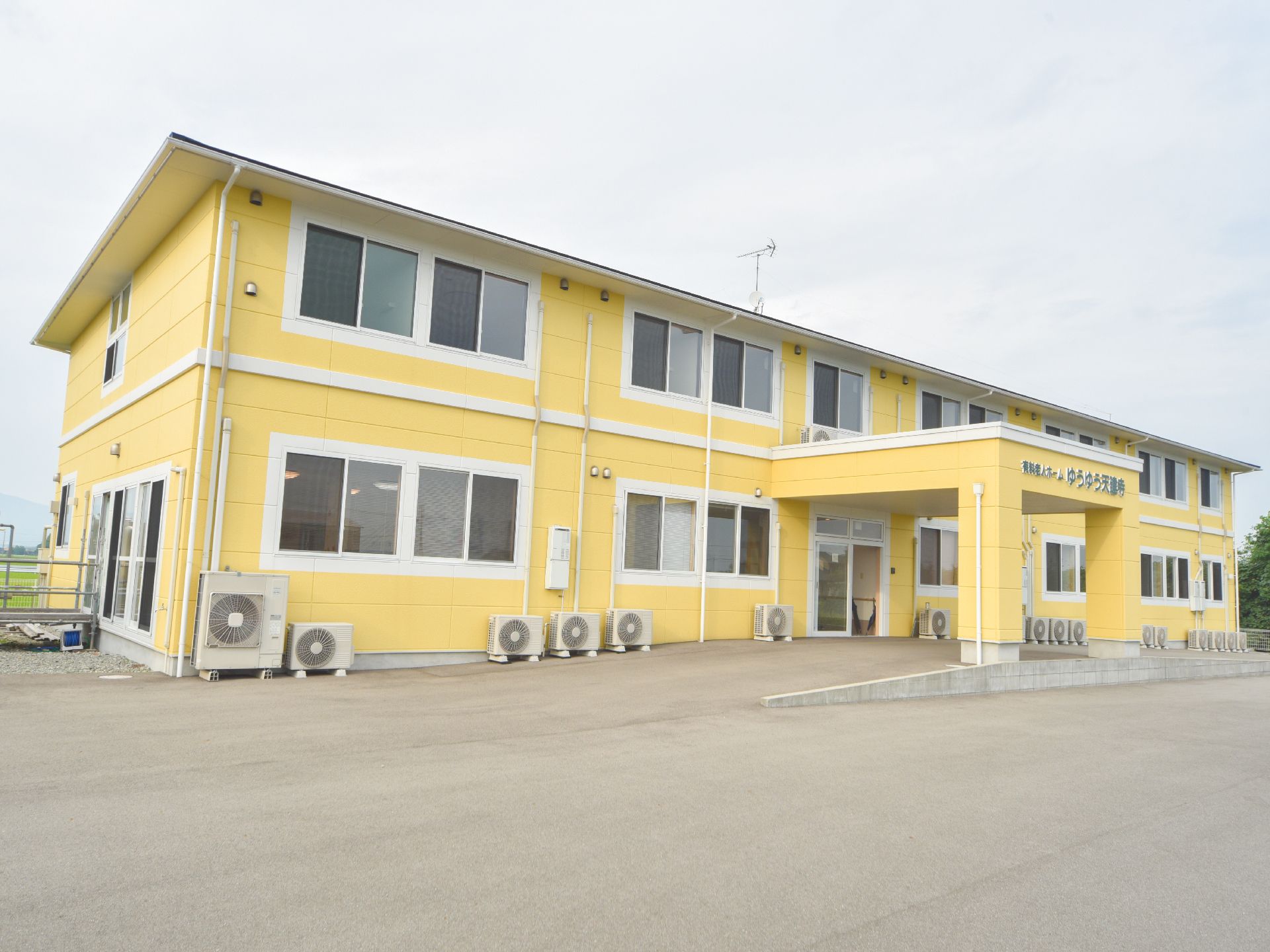 2階建ての施設の前には広い敷地がひろがり、ゆったりとした雰囲気である。遠くに山が見えたりと自然を感じることもできる。
