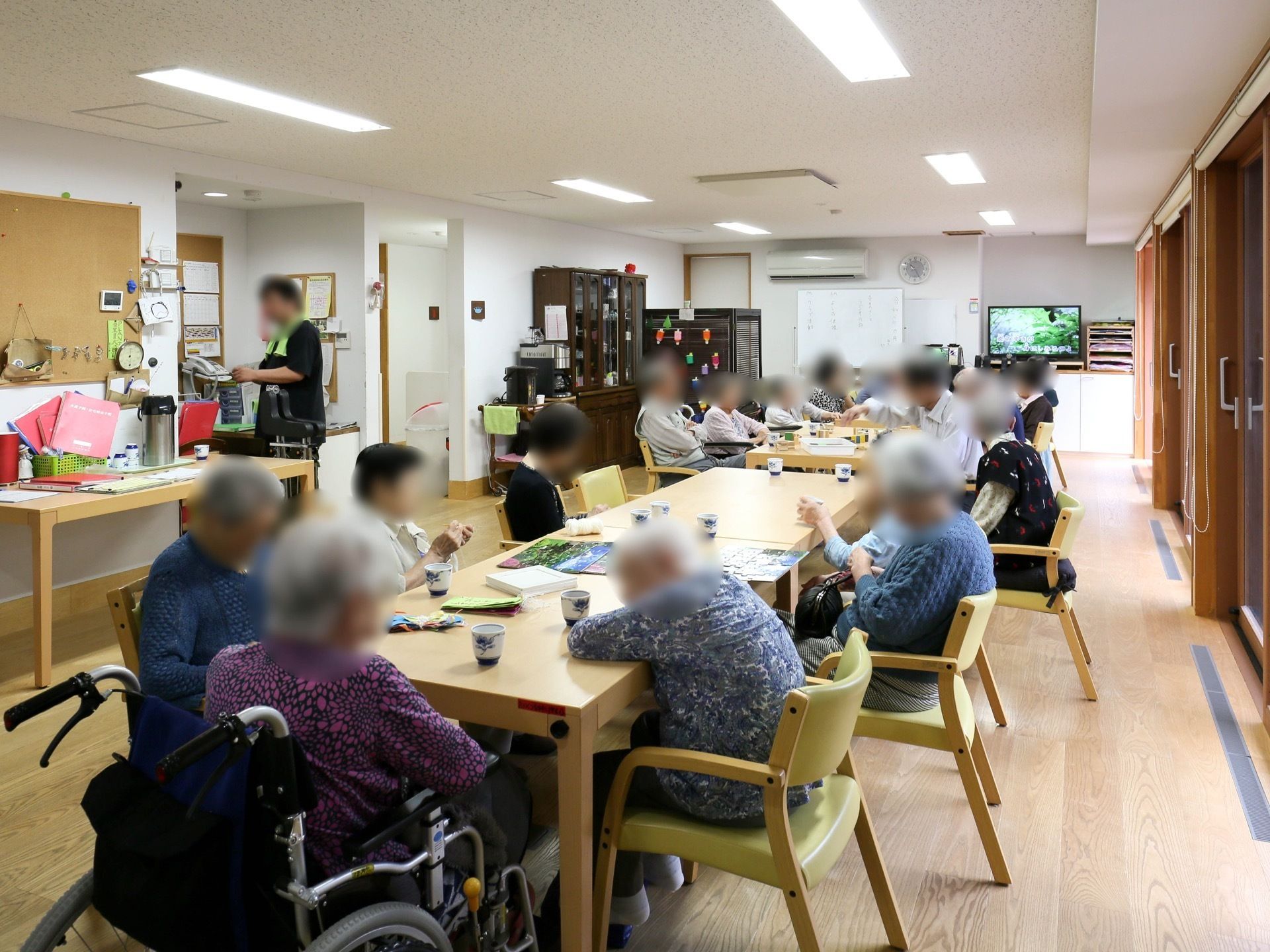 フロア中央にダイニングテーブルのセットが複数セッティングされている。入居者様が机を囲んで、思い思いの時間を過ごしている。