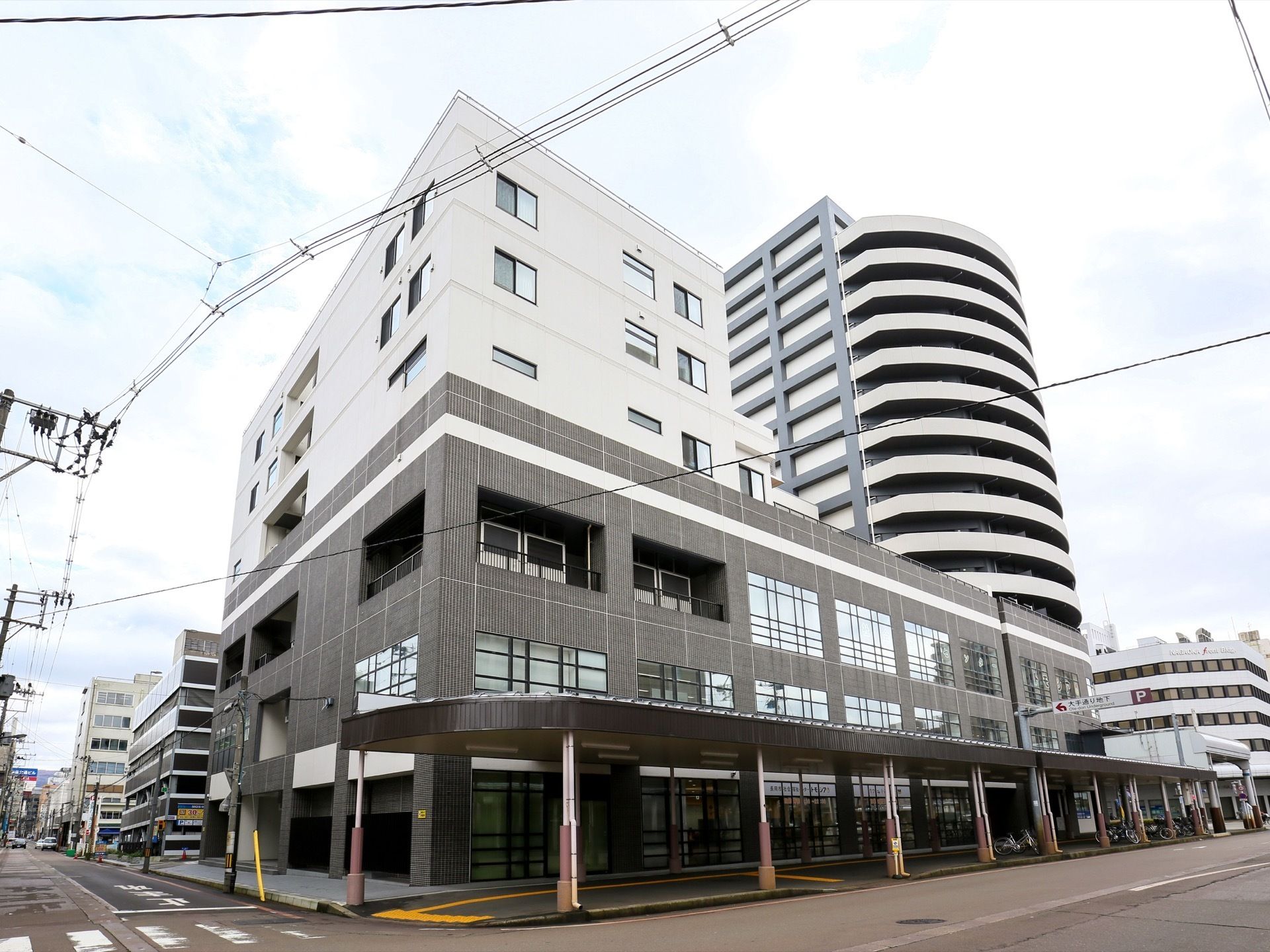 街中に佇む、存在感ある施設である。大通り側には歩道が設けられ、屋根も設置されている。点字ブロックもある。