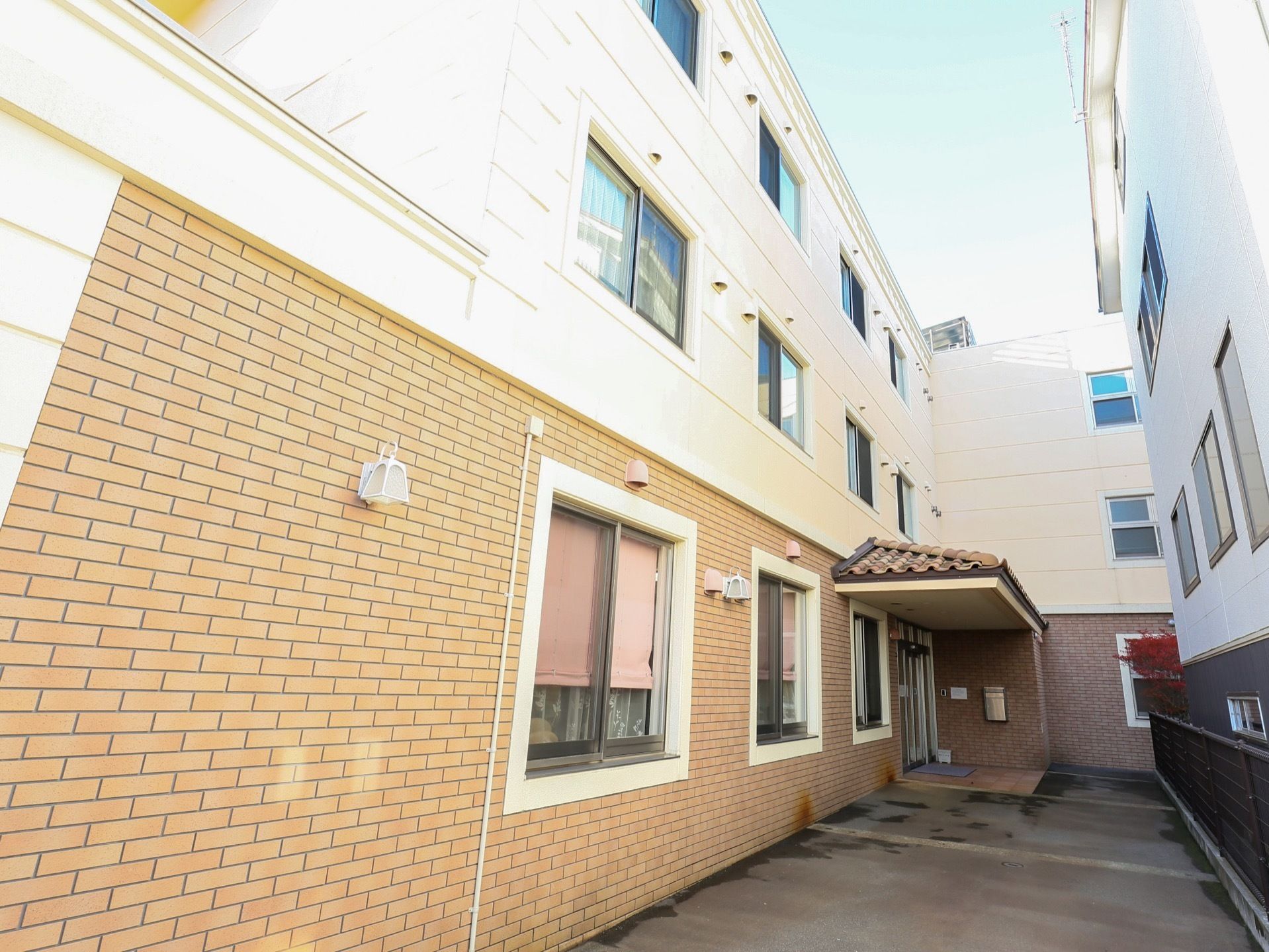 玄関は建物の奥の方にあり、上には屋根が付いている。壁はレンガ調になっていて、小さな照明が付いている。
