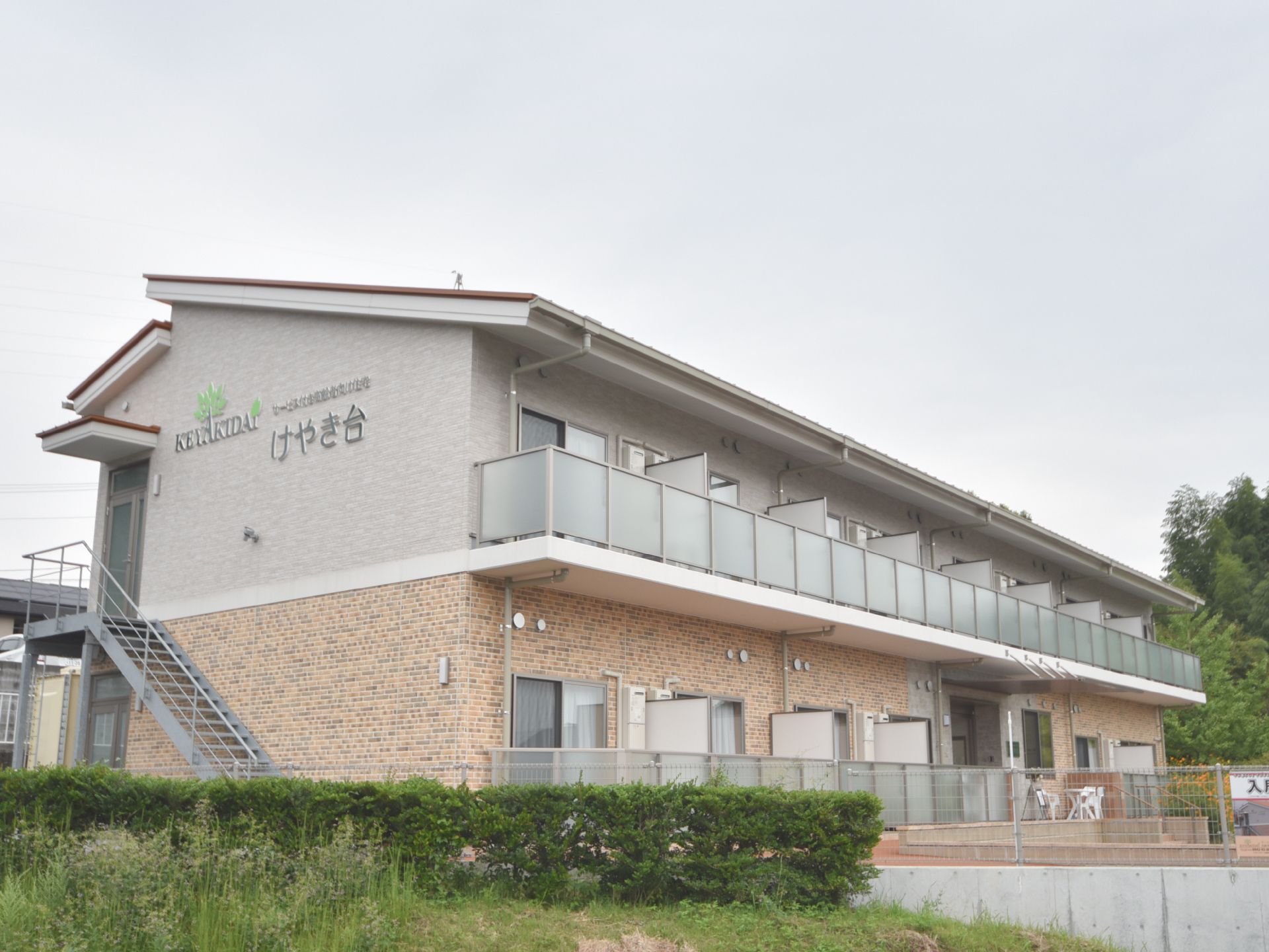ツートンのレンガ調の壁面でまとめた2F建て。全部の部屋に自然光の入る横長の建物。二階壁面に施設名が入っている。