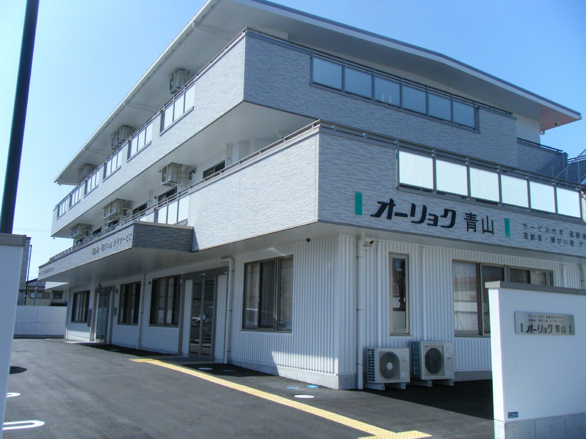 外壁が白とグレーで統一された、シンプルな3階建ての建物
