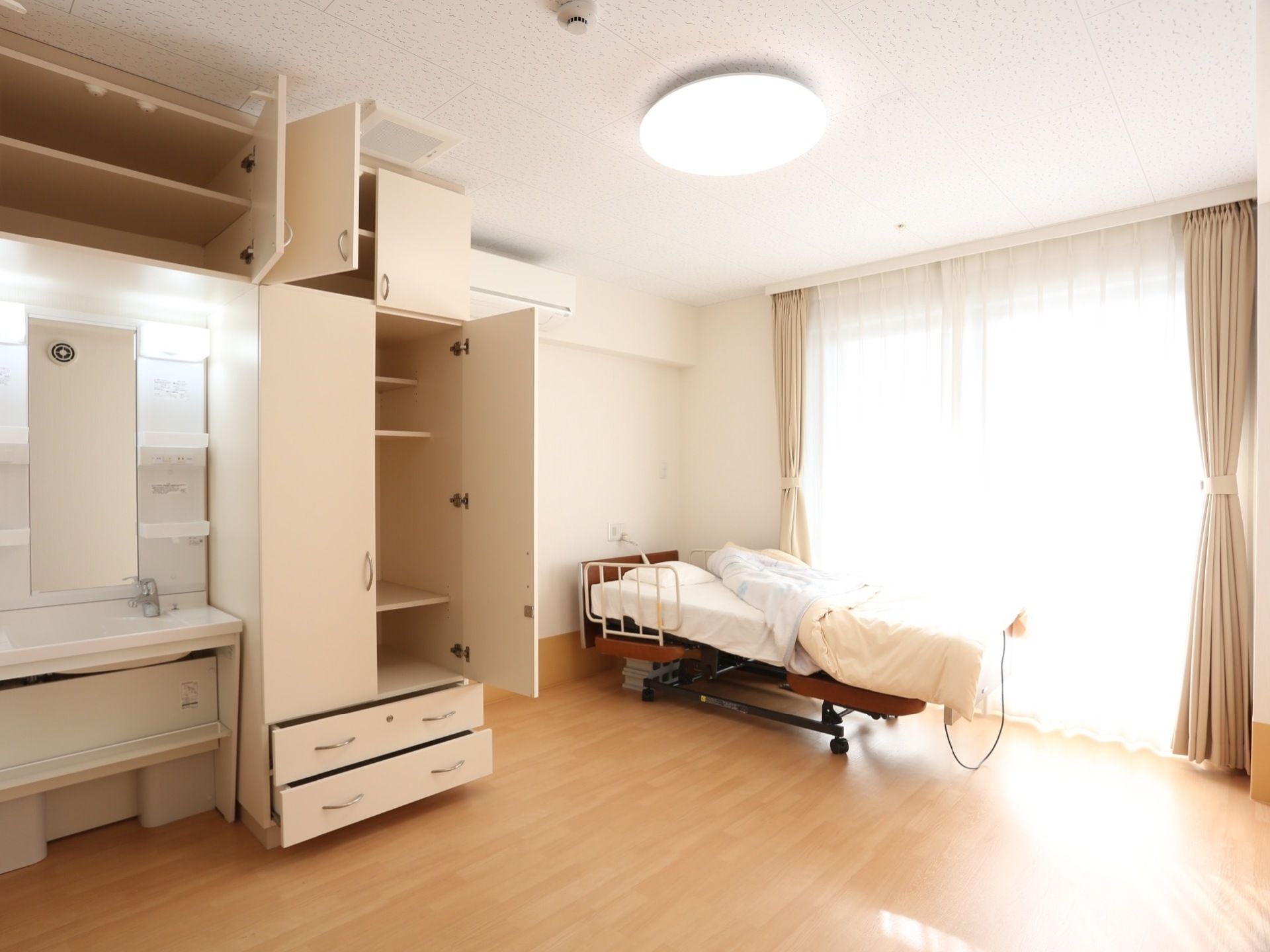 広々としたフローリングの個室に、介護用ベッドが置かれている。クローゼットが設置されており、窓にはカーテンが掛けられている。