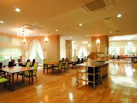 背もたれの高いグリーンの椅子がセットされたダイイングテーブルが複数並び、大きな窓の外には緑が広がっている。