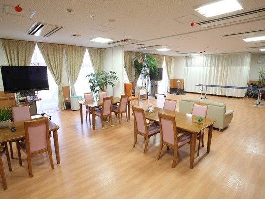 4人掛けのダイニングテーブルが複数置かれた食堂スペースが手前にあり、奥には平行棒やソファが置かれている。
