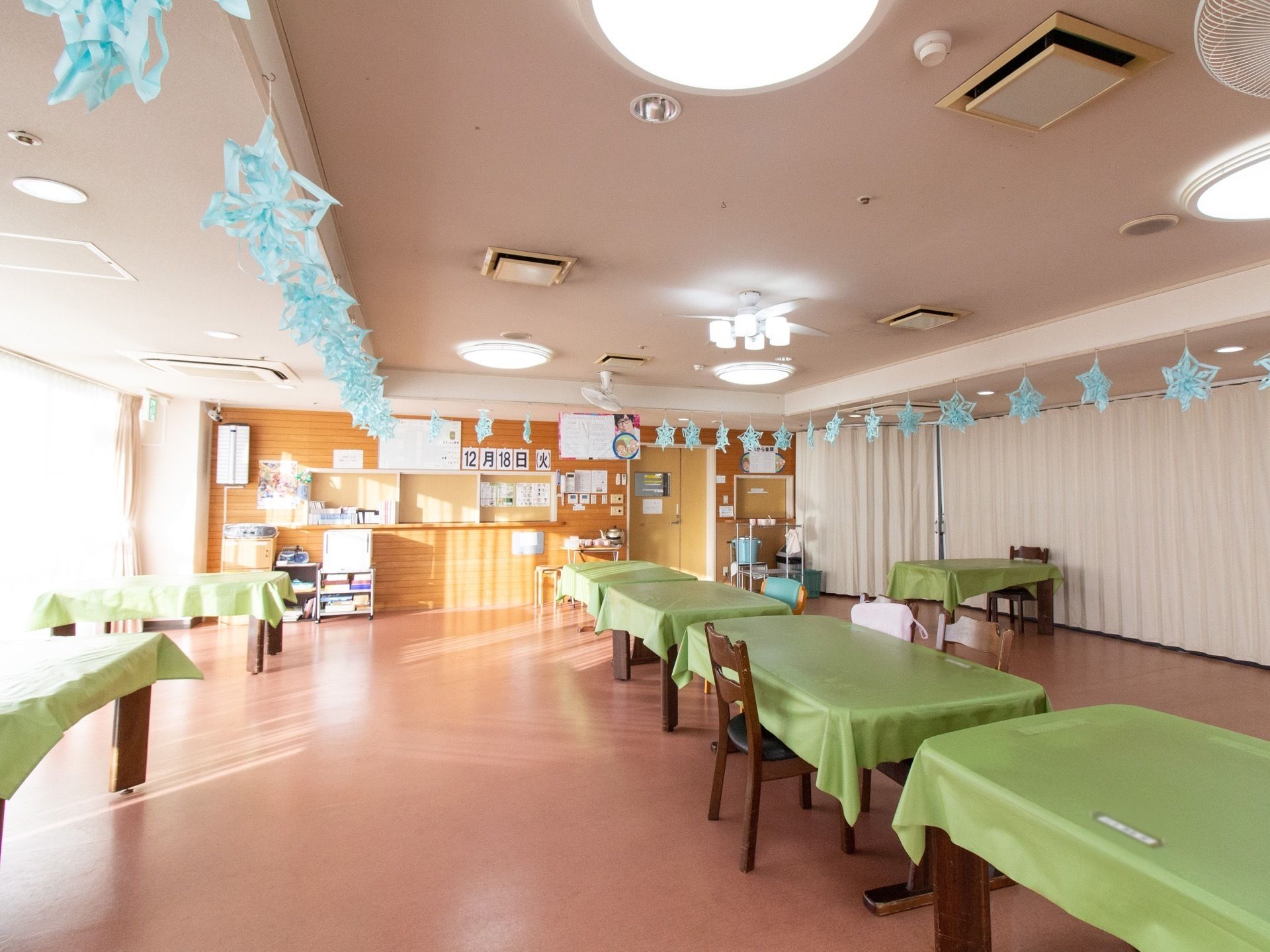 大きな窓から外の光が差し込む広々とした食堂。各食卓の上にはテーブルクロスが敷かれており、天井には手作りの装飾が施されている。