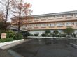 アスファルトで舗装された敷地に、植栽で囲まれた3階建ての住宅が建っている。建物の前は駐車スペースになっている。