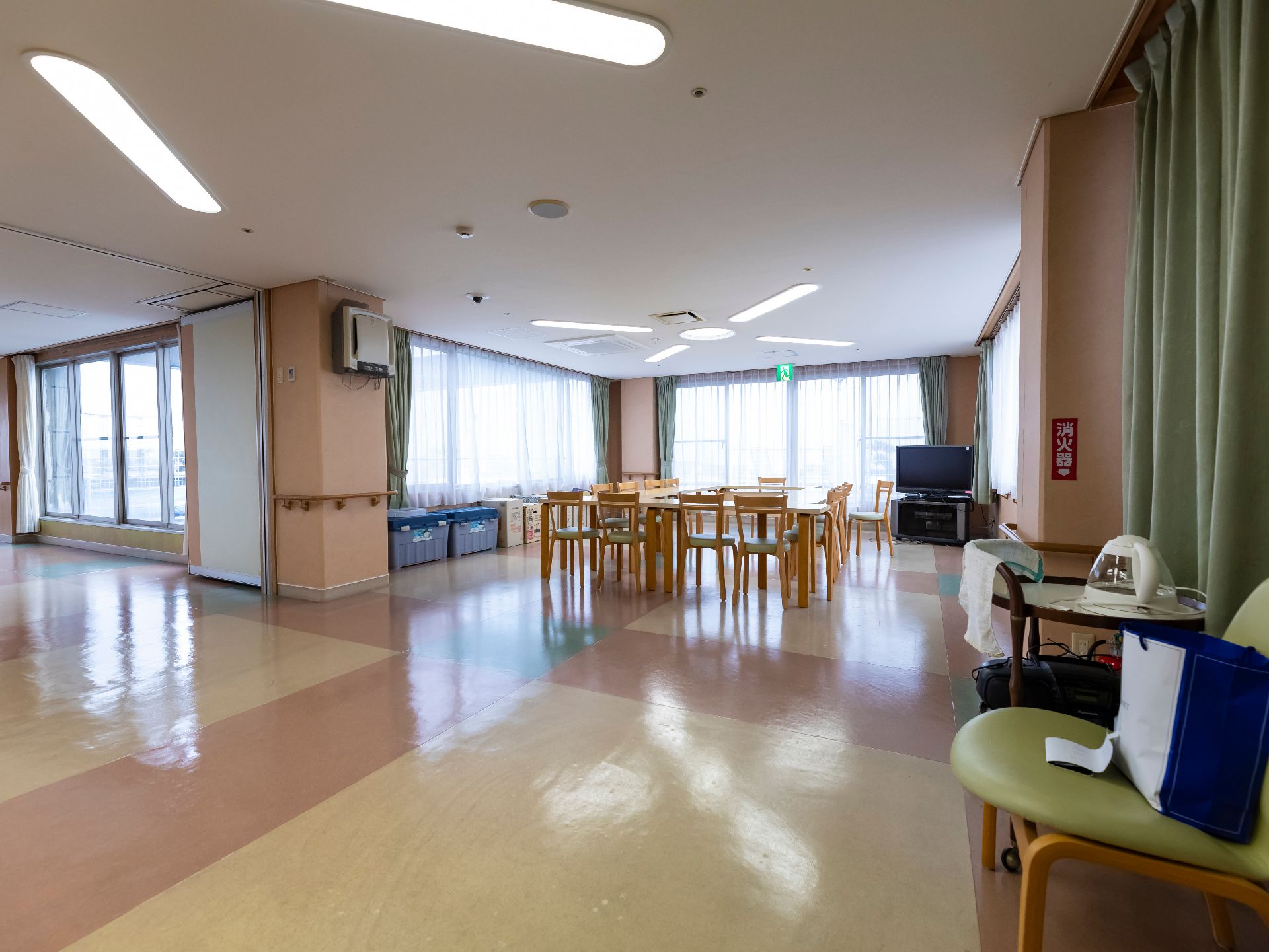 壁一面が窓ガラスの広間に置かれたテレビと対面した机と椅子