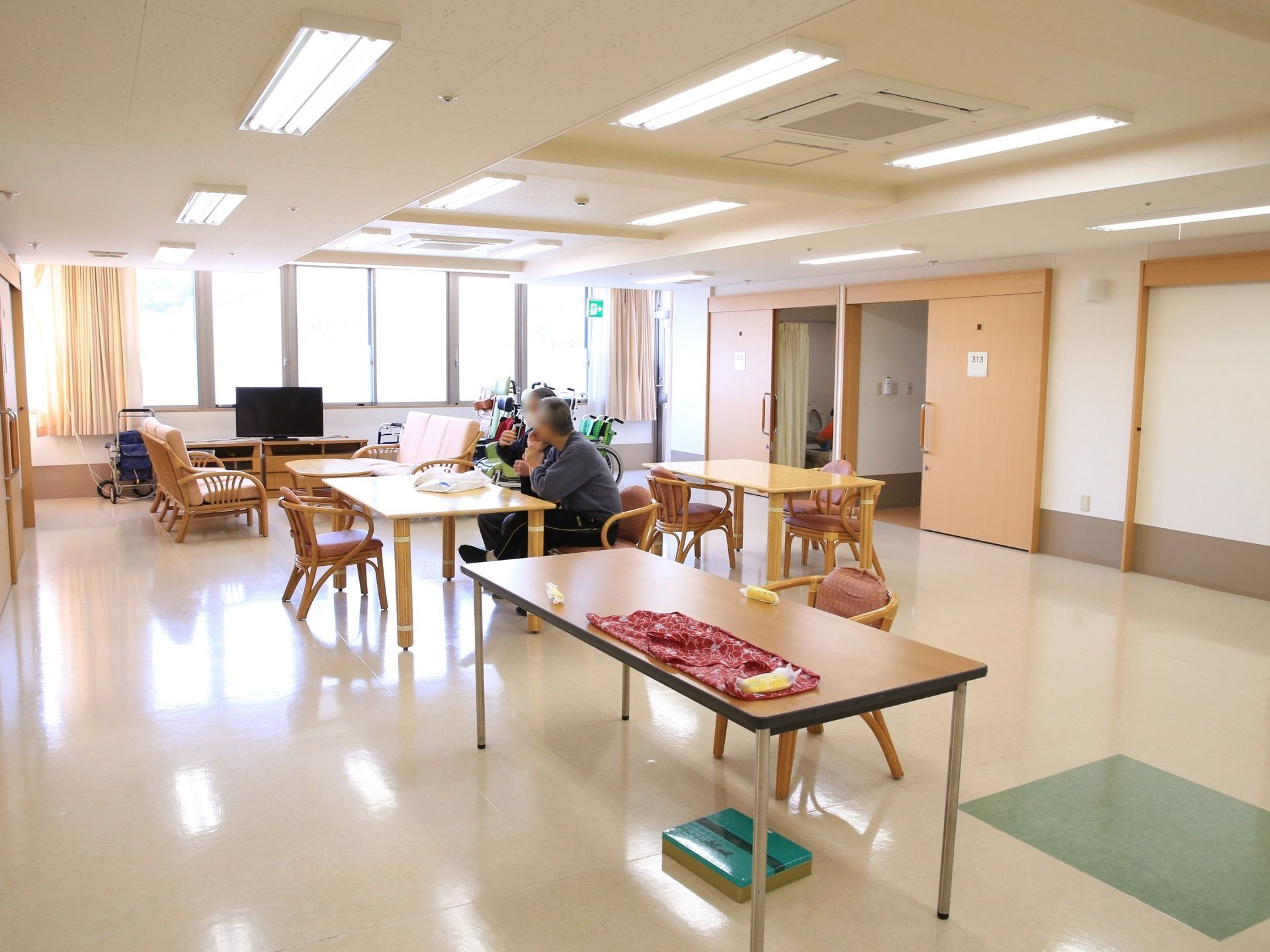 広々とした共有スペースには大きな窓が設けられており、外光がしっかりと入ってきている。部屋にはテーブルや椅子、テレビなどが設置されている。