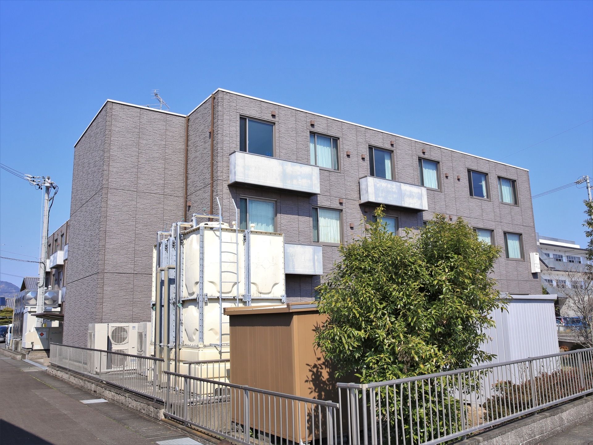 日差しを遮るような高い建物などが周囲にない敷地に建つ３階建ての施設である。敷地境界にはフェンスが立てられている。